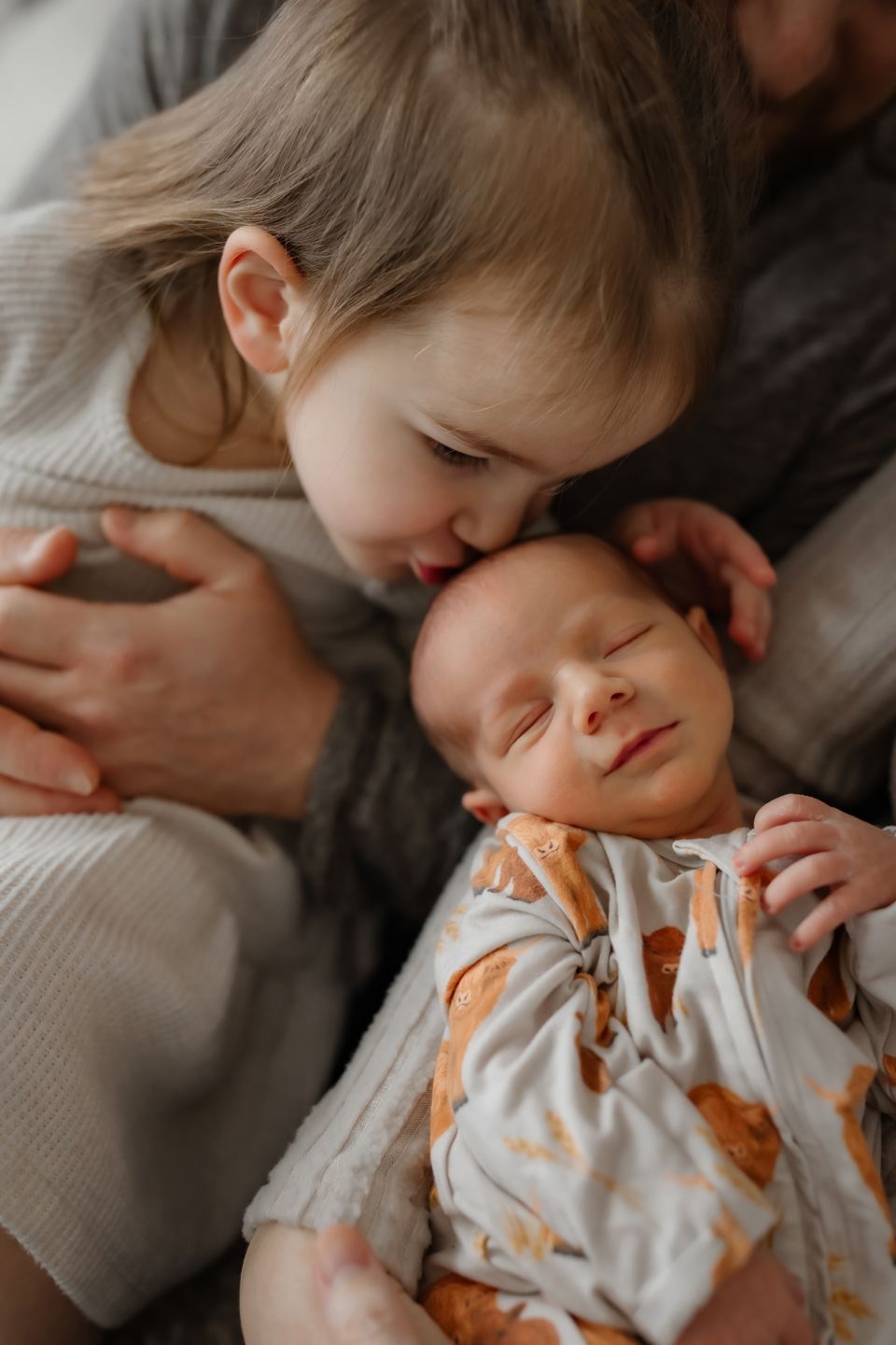 Tender family moment showing siblings sharing a gentle embrace on soft bedding.