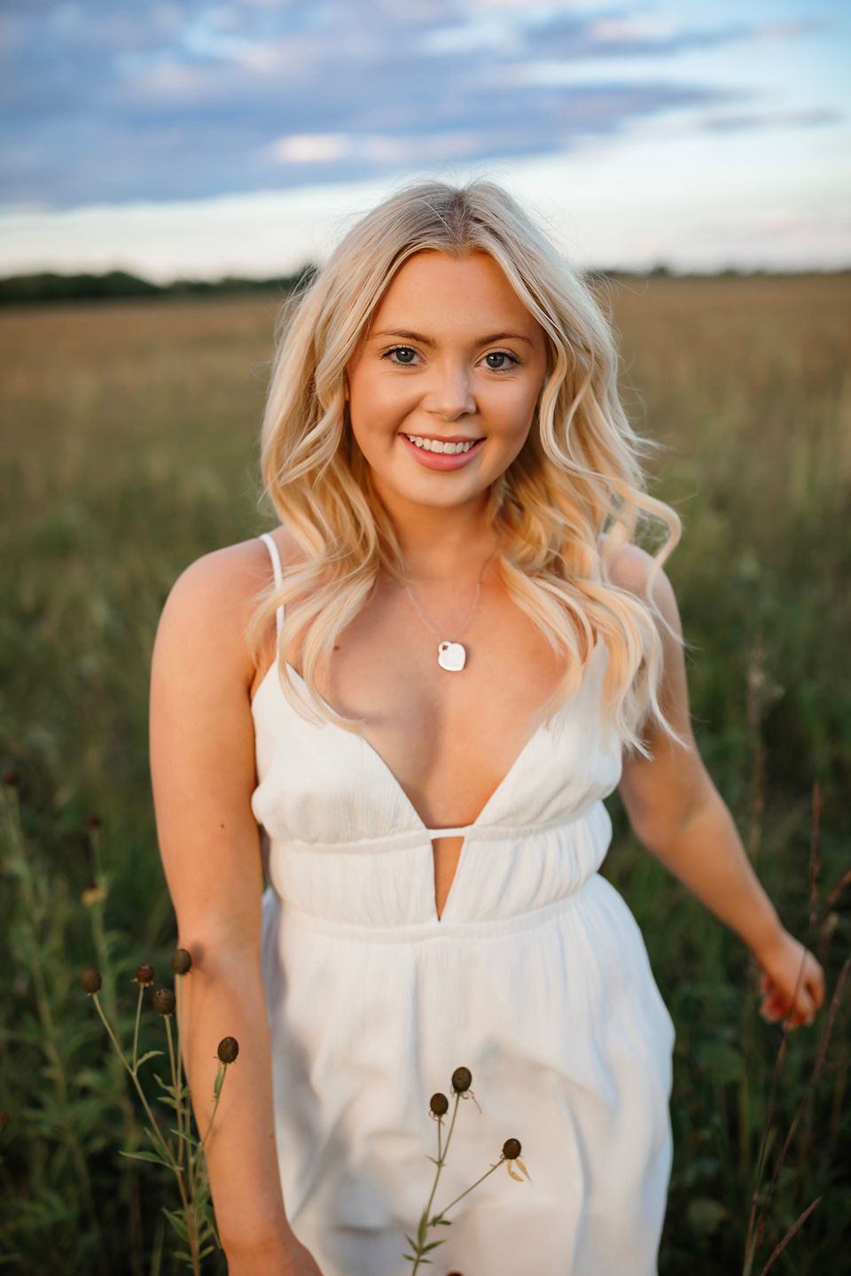 Summer portrait in white dress standing in wildflower field at sunset.