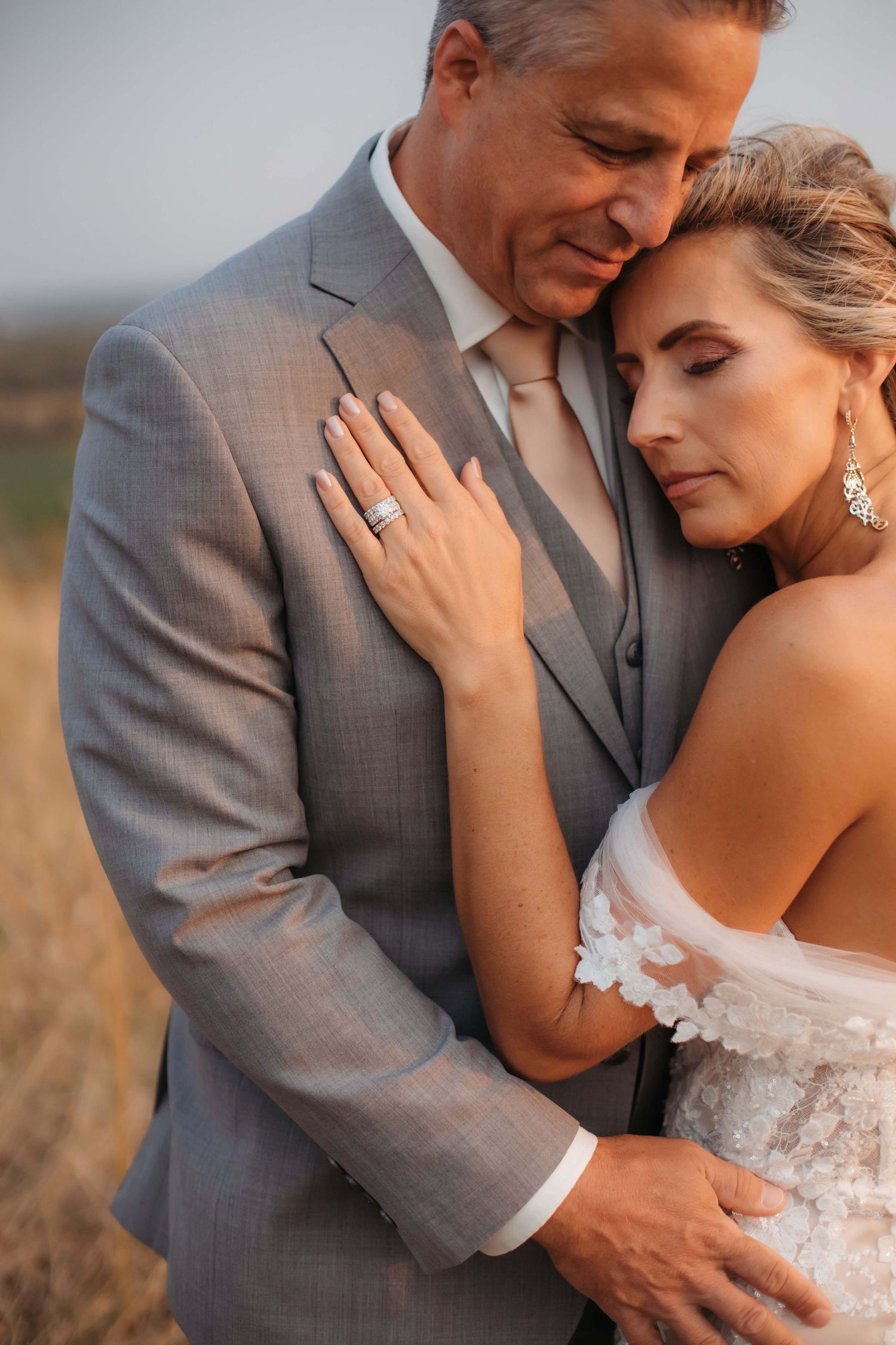 Intimate wedding portrait showing detail of diamond ring and lace dress against golden sunset backdrop.