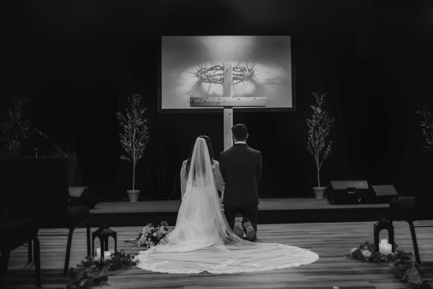 Black and white photo of newlyweds sitting at altar with projection screen during wedding ceremony.
