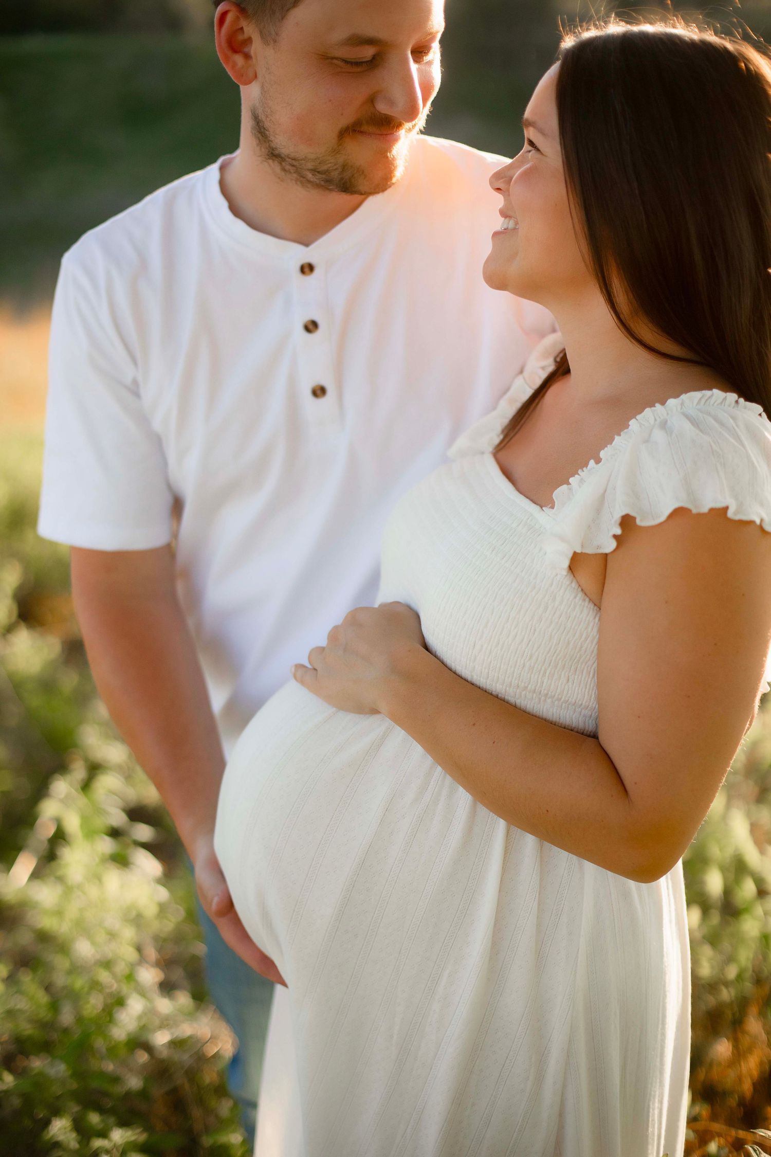 Pregnant couple sharing tender moment outdoors in warm golden sunset light.