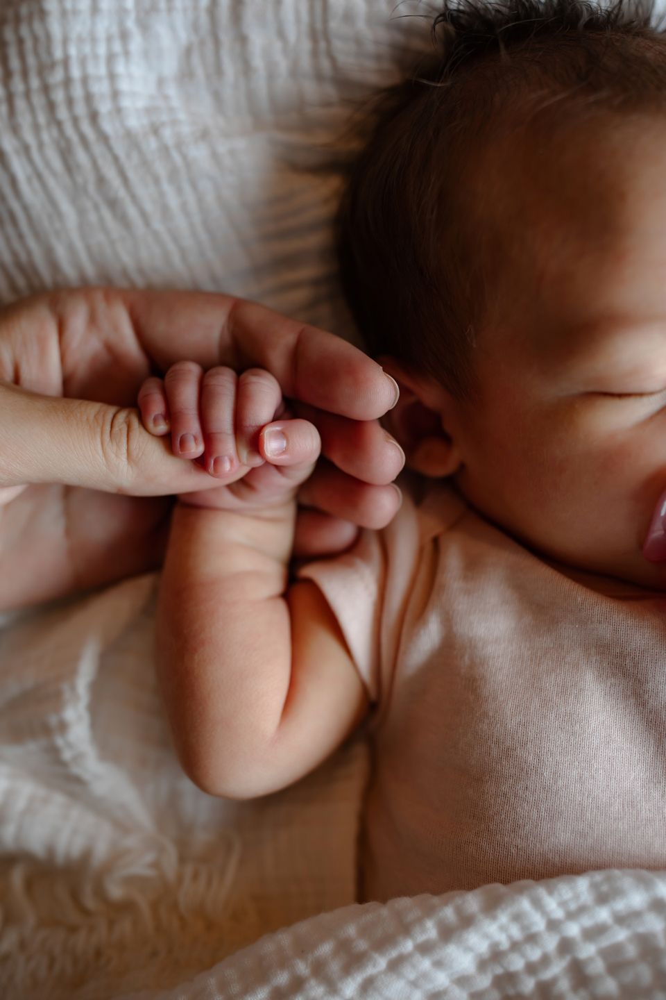 Close-up of newborn's tiny hand being held against white bedding.