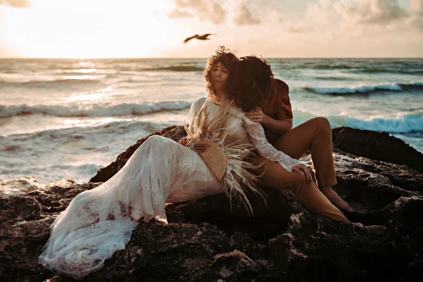 Intimate seaside moment on rocky beach in Tulum with waves crashing in background.