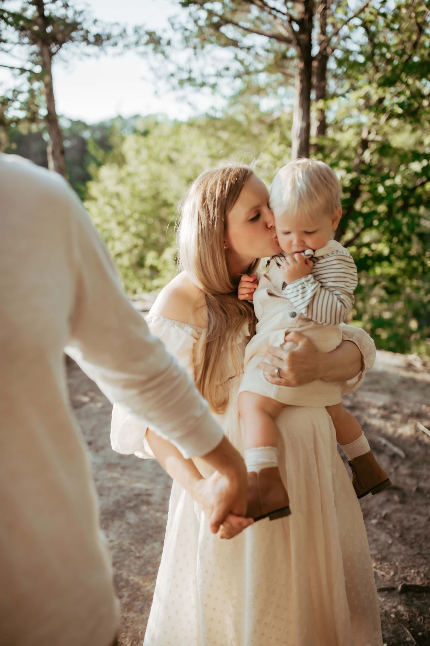 A gentle family moment captured outdoors with warm sunlight filtering through trees in the background.