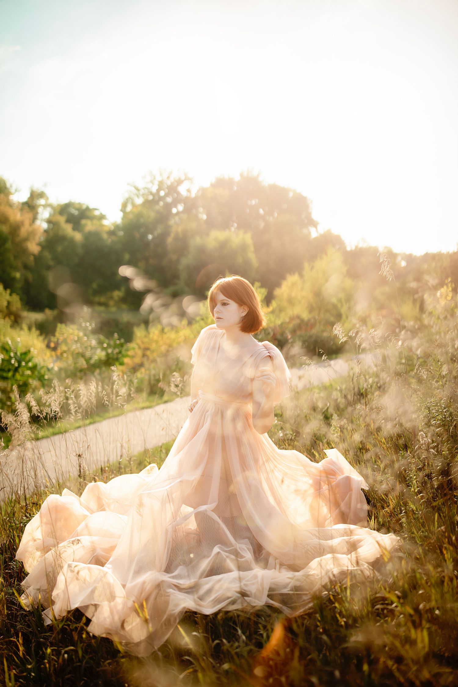 Person in flowing peach dress twirls in golden sunlit field at sunset.