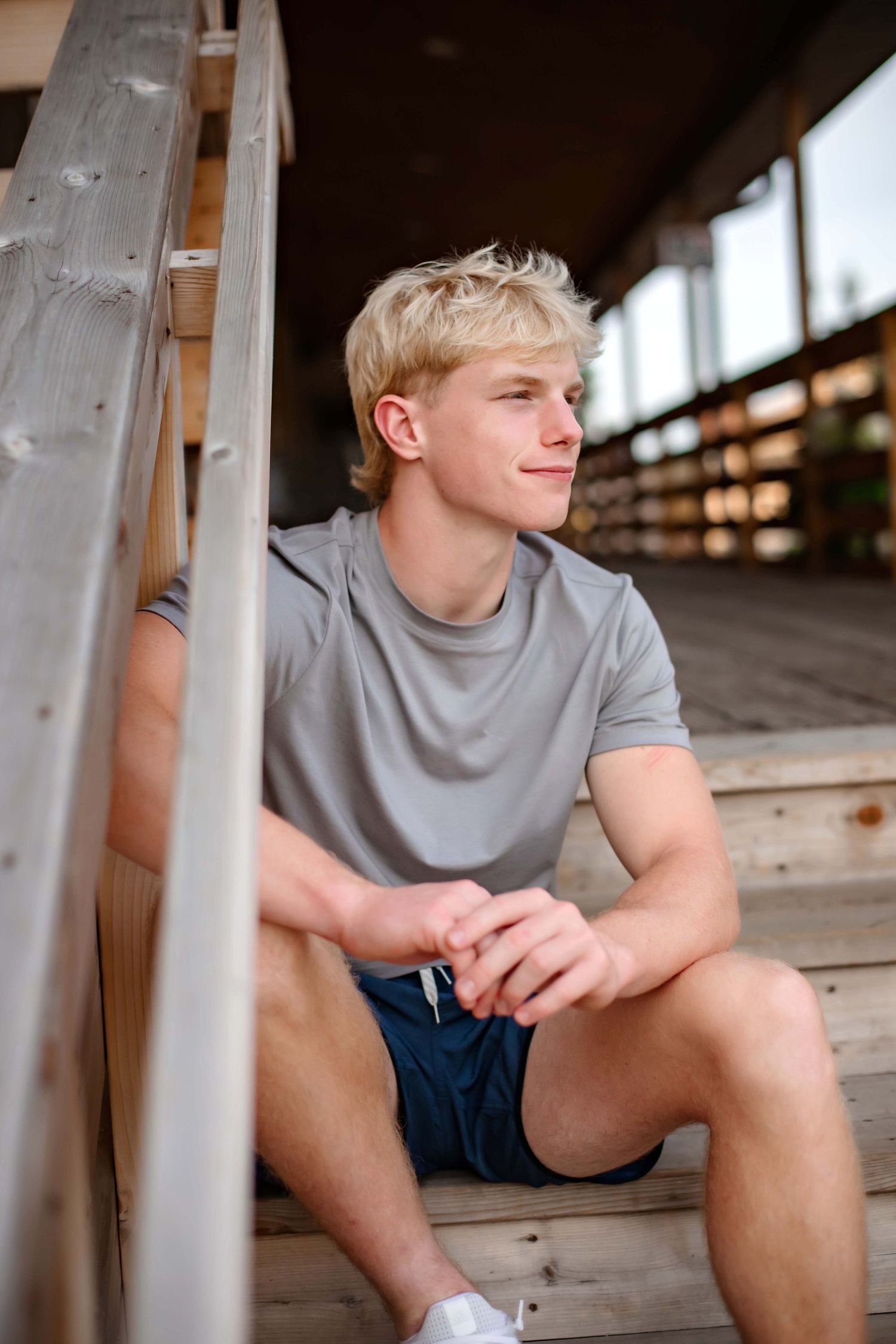 Person resting thoughtfully on wooden deck stairs in gray t-shirt.