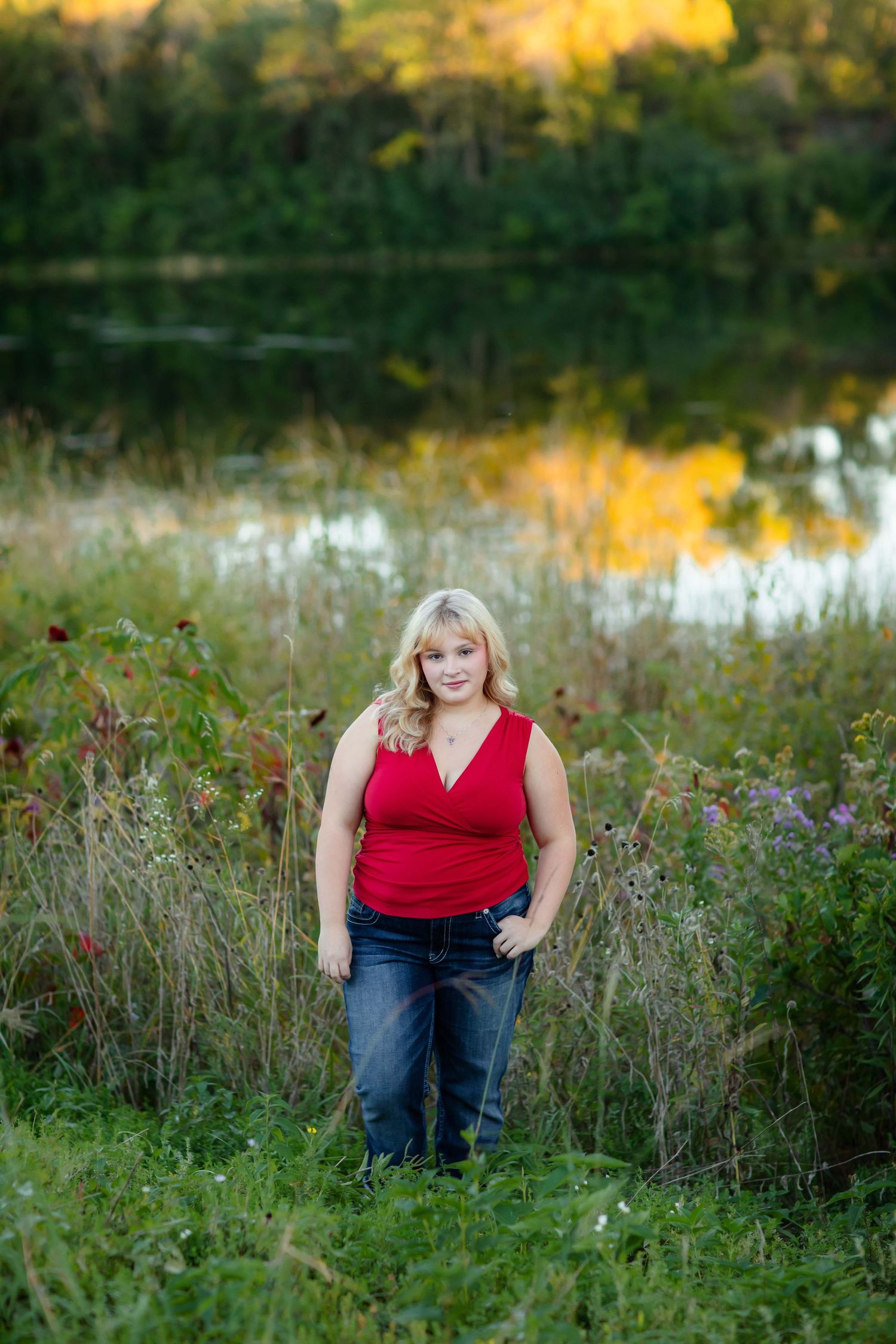 Portrait by lake at sunset with tall grass and wildflowers.