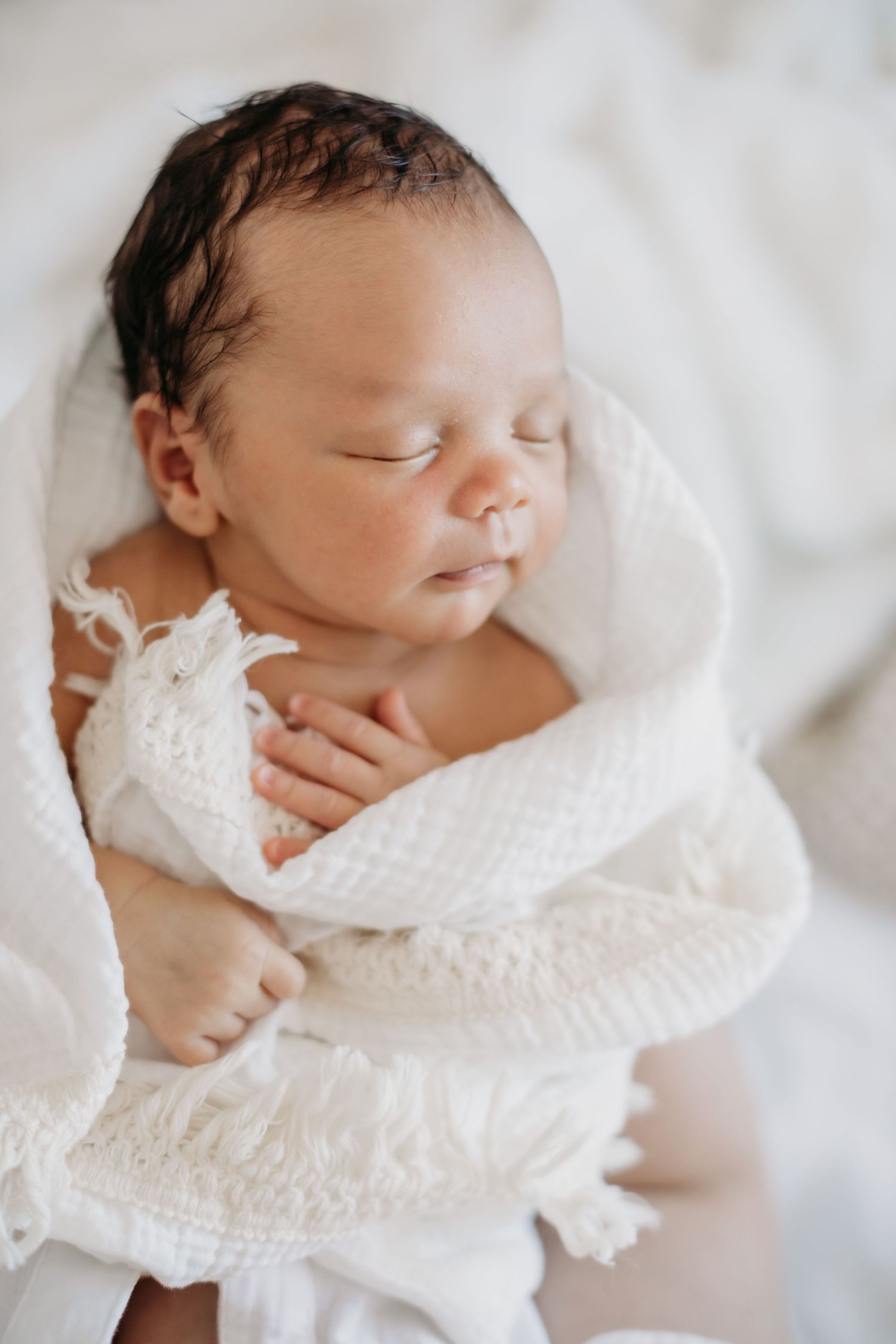 Close up of peaceful sleeping newborn wrapped in delicate white fabric.