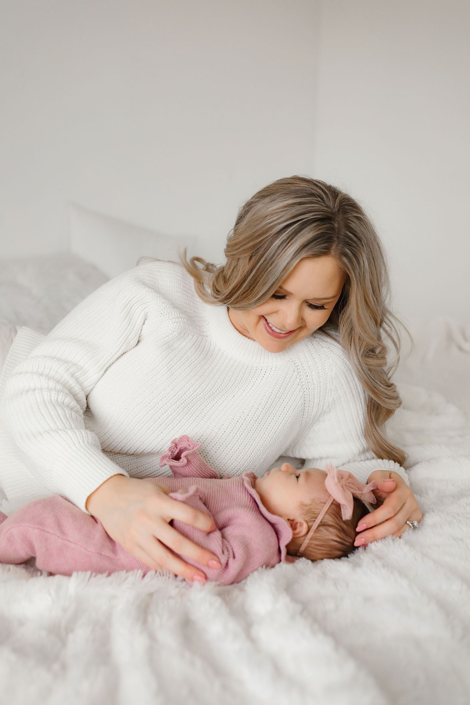 Person in white sweater snuggling with baby on soft bedding.