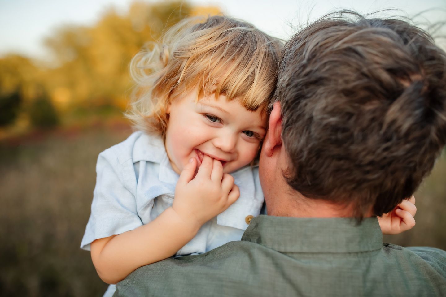 A child being held by an adult during a warm outdoor sunset with a blurred natural background.
