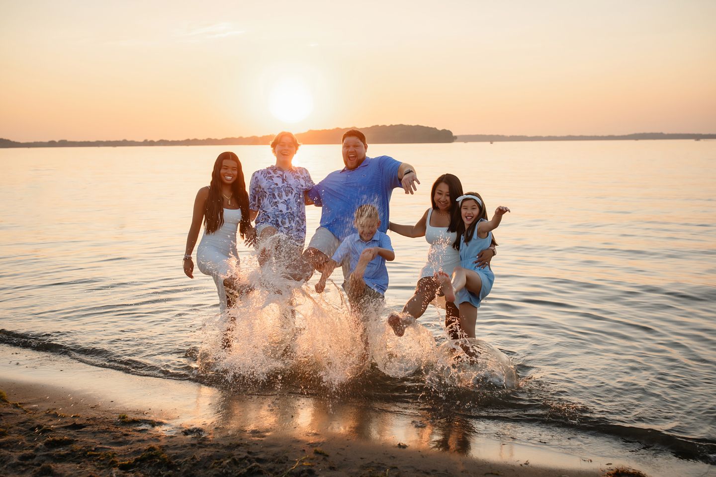 People splashing water and having fun together at sunset on a beach with calm waves and golden sky in background.