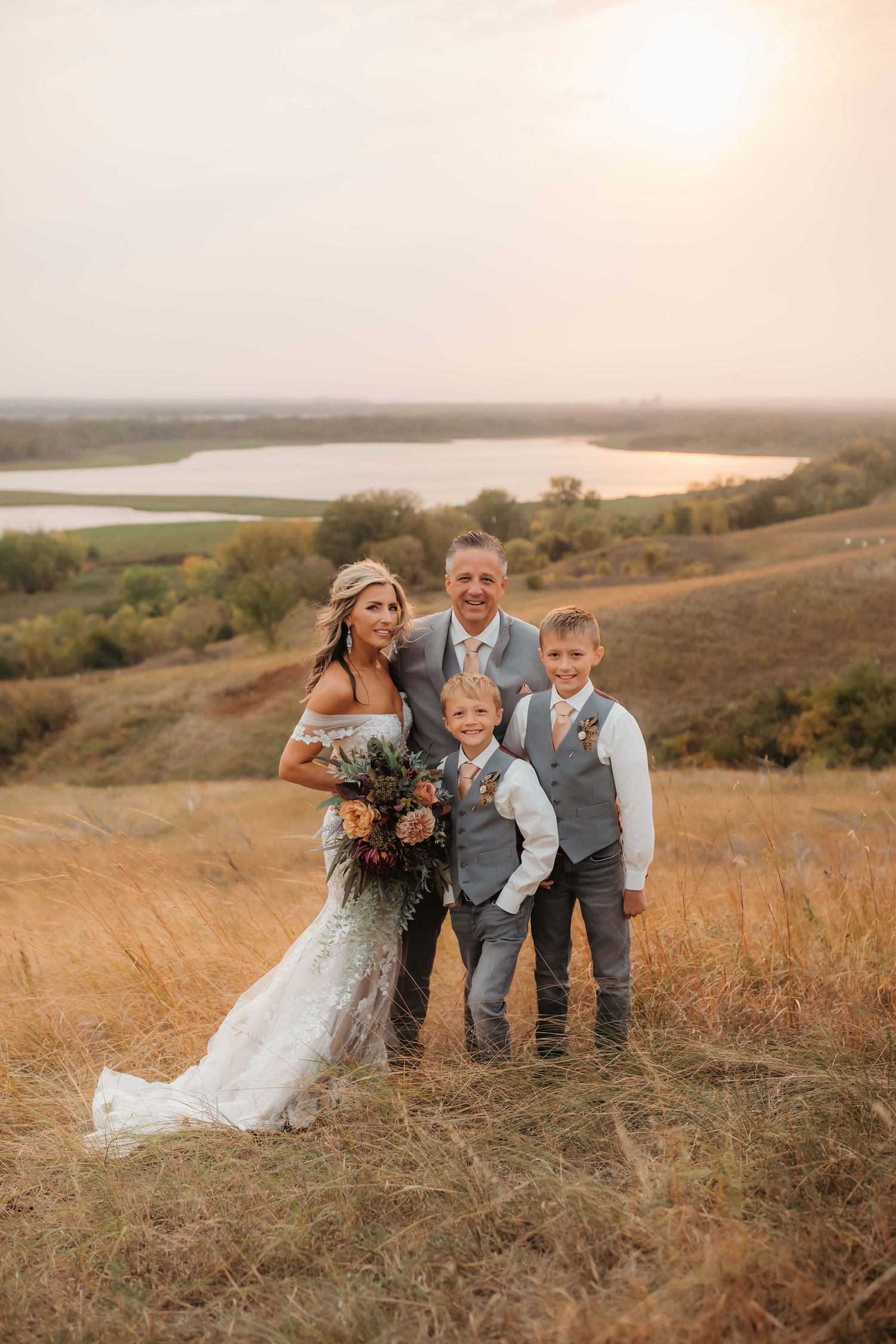Family wedding photo with couple and children against sunset landscape.