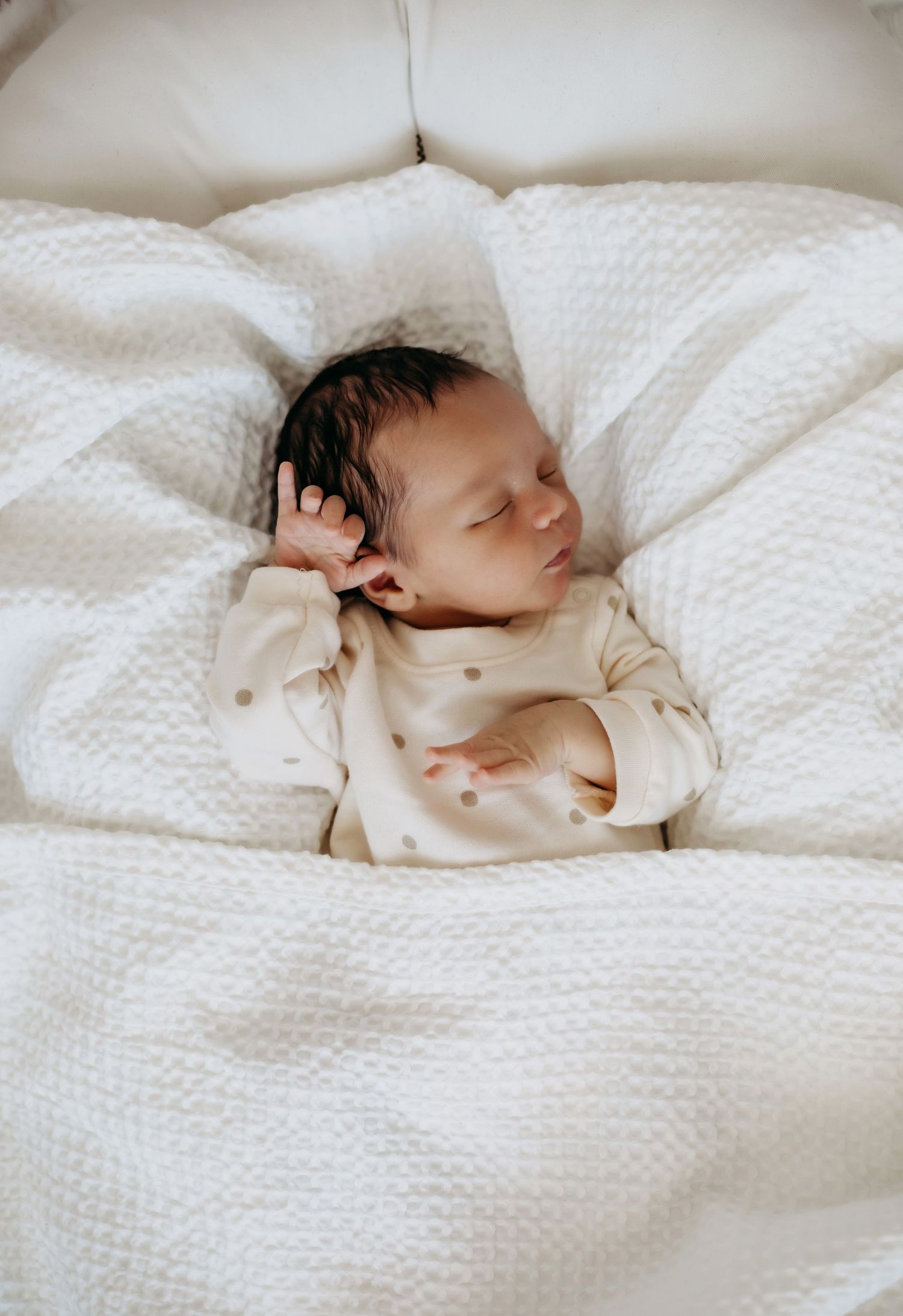 Peaceful sleeping newborn in polka dot outfit on white textured bedding.