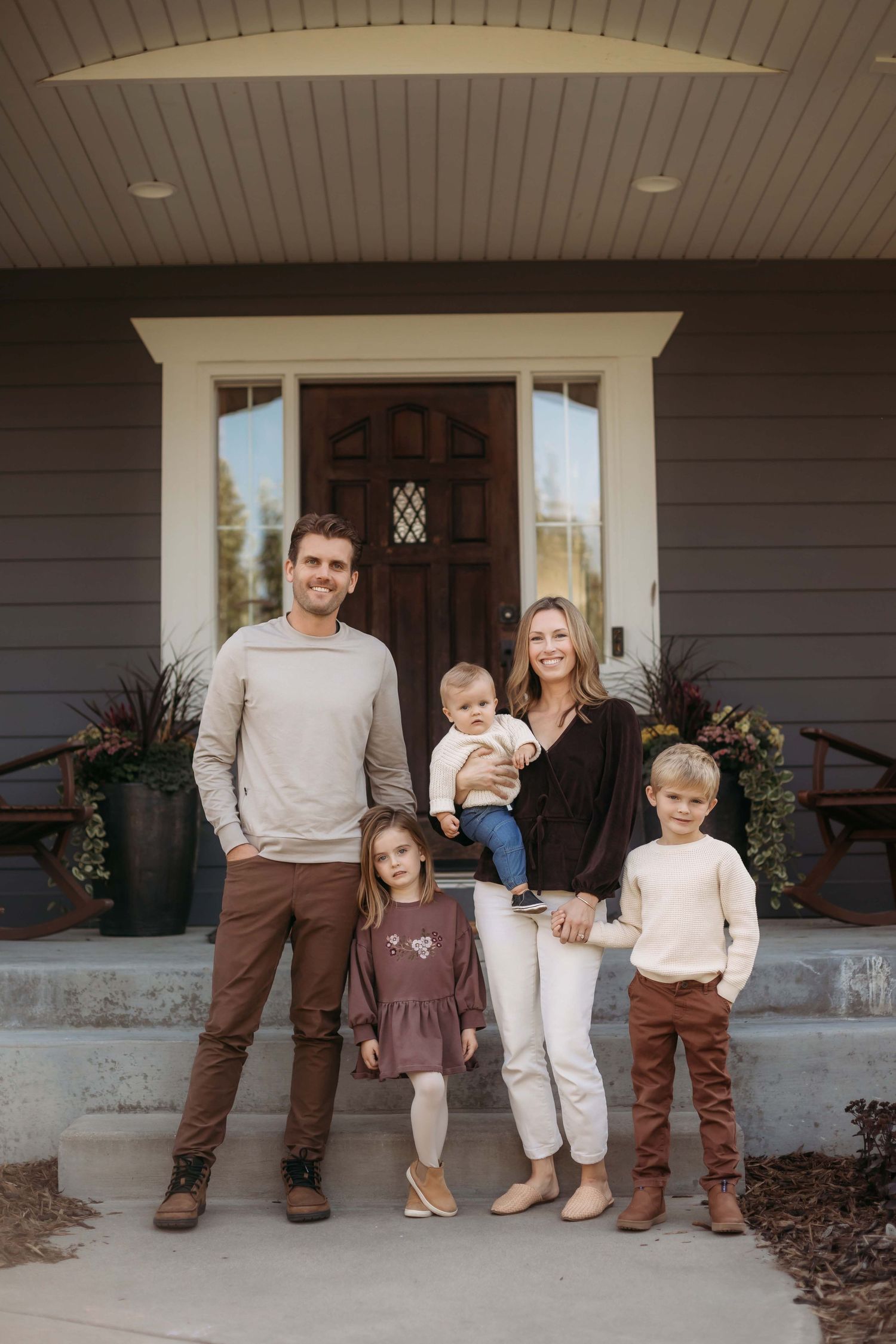 Family of five posing together on their front porch steps of a gray house.