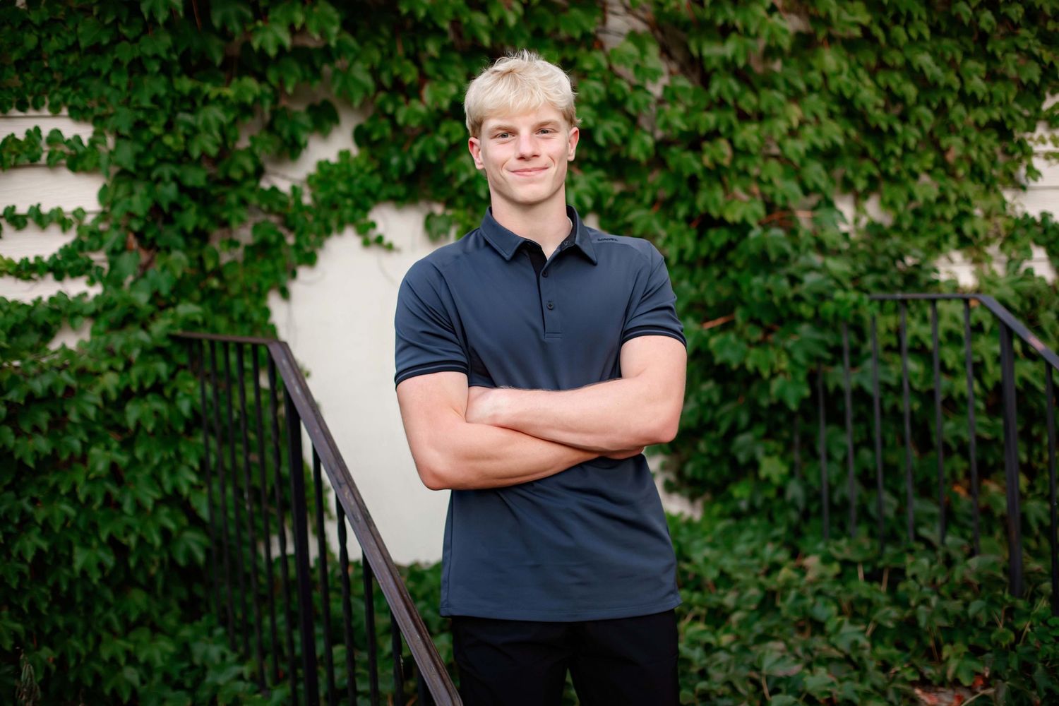 Portrait against ivy wall with arms crossed wearing navy polo shirt.