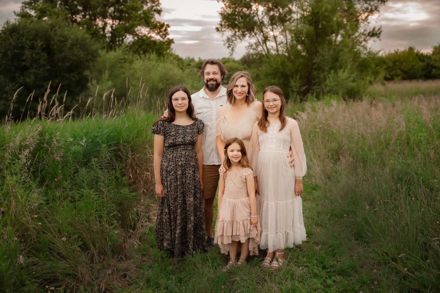 A family of five poses together in a field of tall grass during golden hour.