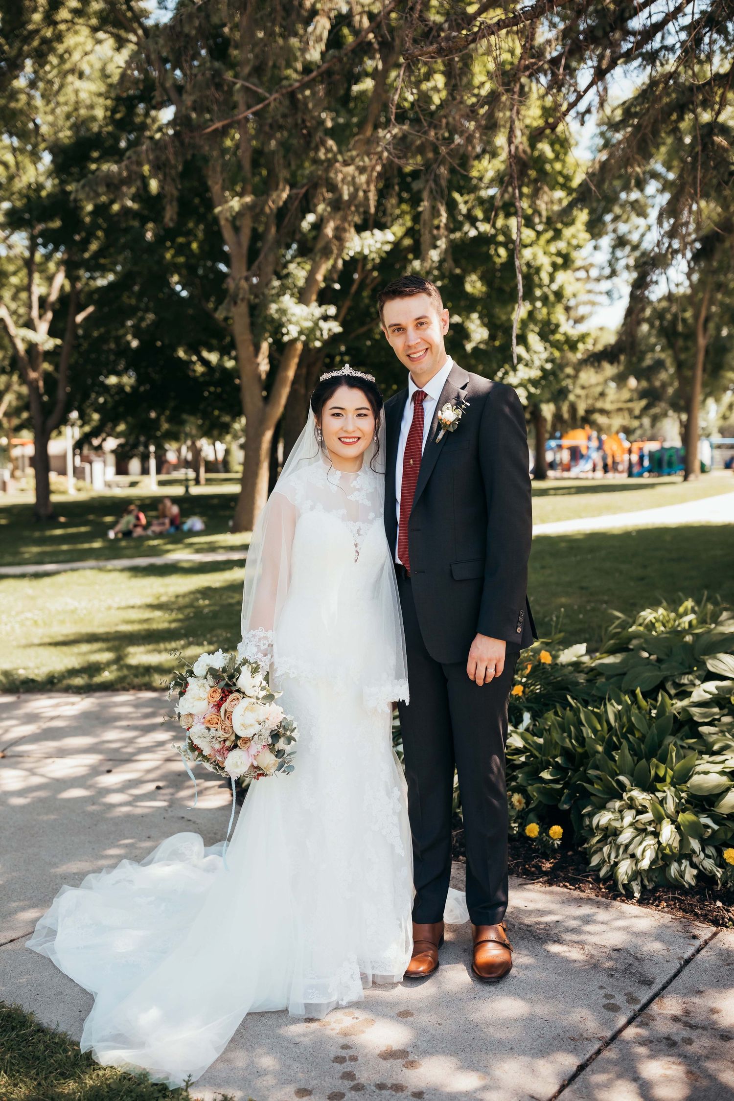 Newlyweds pose together in a sunny garden setting with the bride wearing a flowing white gown.