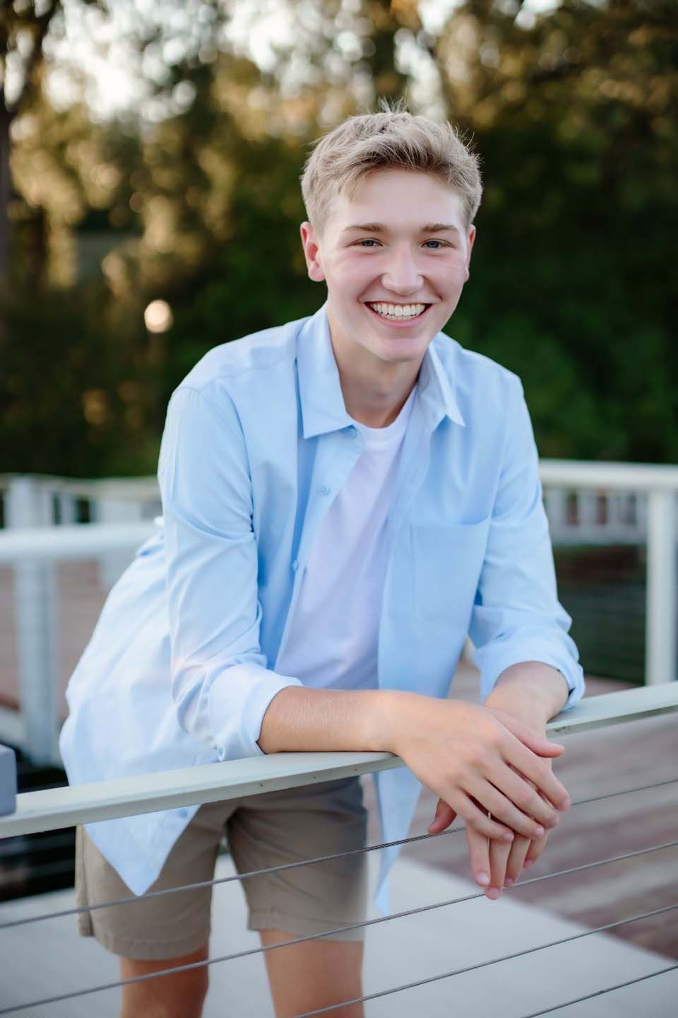 Candid outdoor portrait wearing light blue shirt leaning on deck railing.