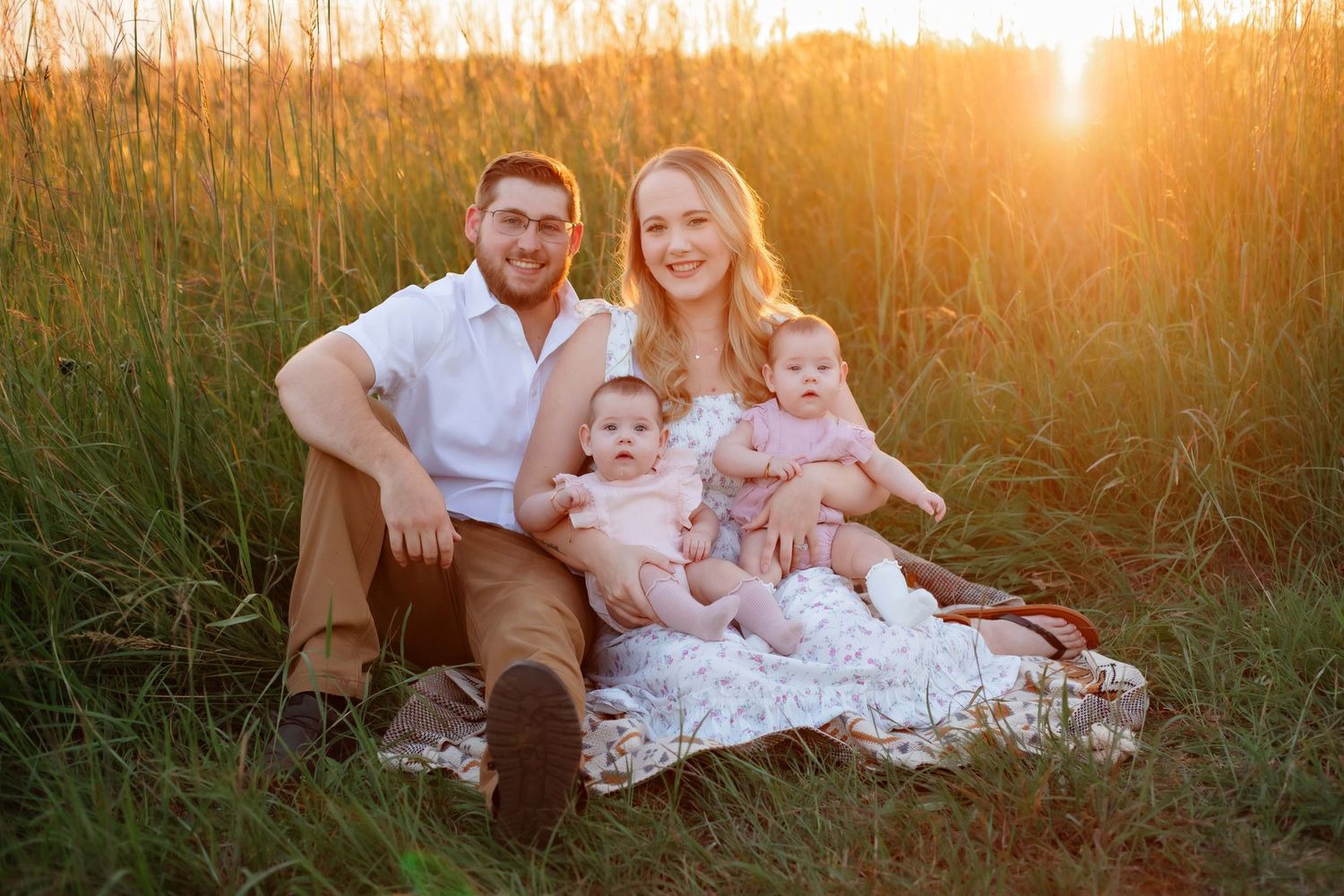 A family relaxes on a blanket in tall grass during golden hour.