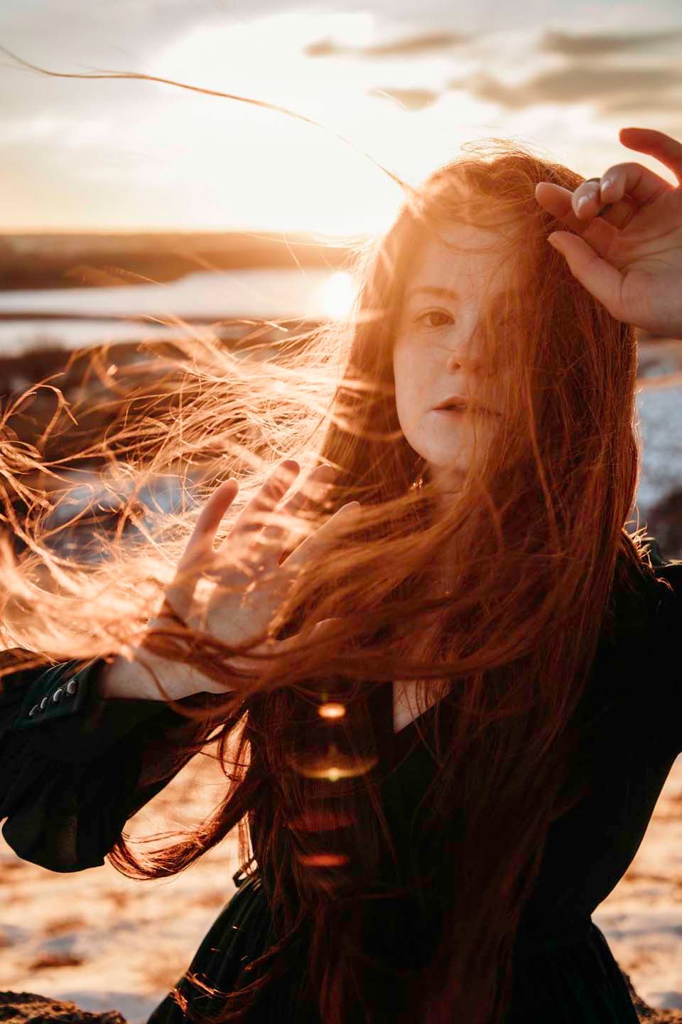 Red hair blowing in ocean breeze during golden hour sunset.