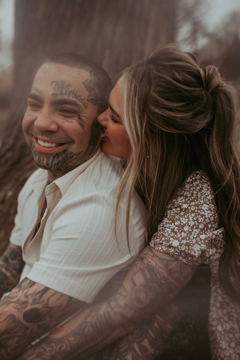 A couple sharing an intimate moment together wearing white and floral clothing with visible tattoos.