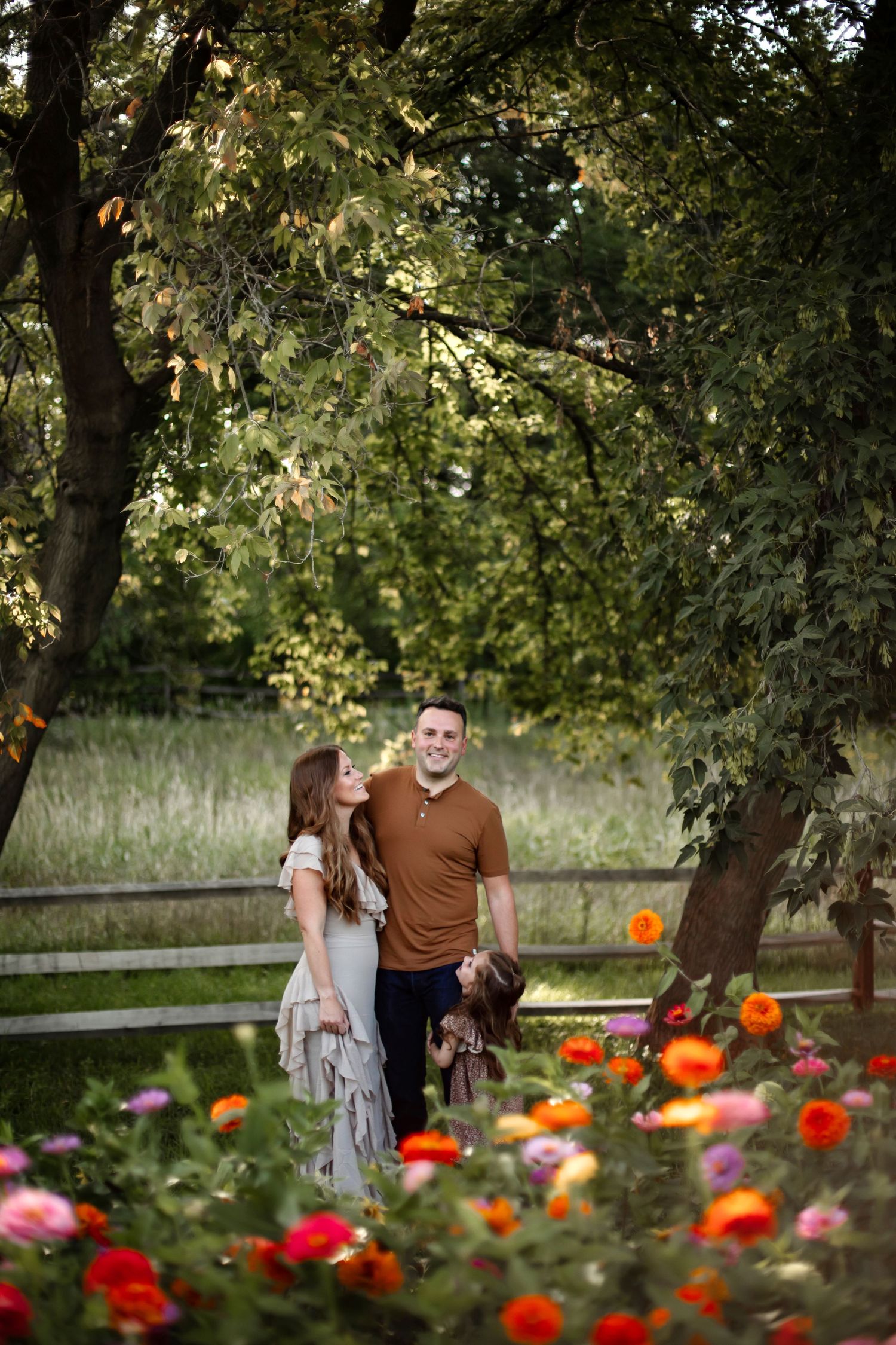 Couple standing together in garden with bright orange and red flowers blooming in foreground on sunny autumn day.
