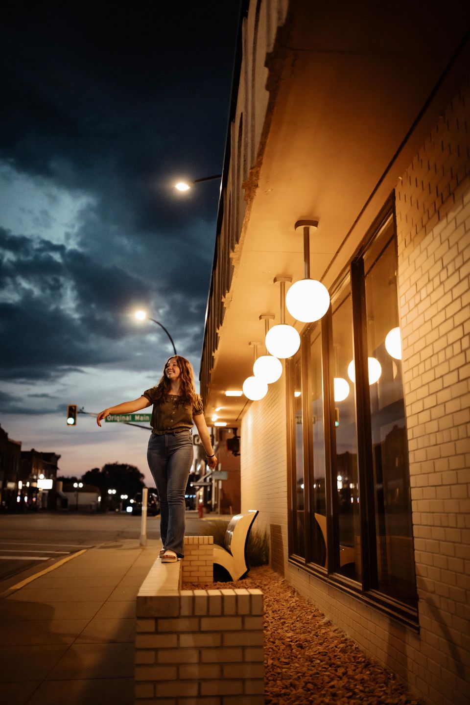Person balancing on ledge at night with glowing street lights and dramatic sky.