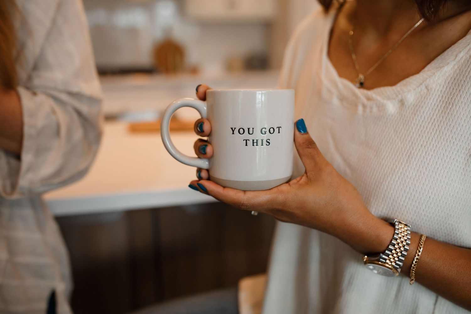 Hands holding a white ceramic mug with motivational text in a modern kitchen setting.