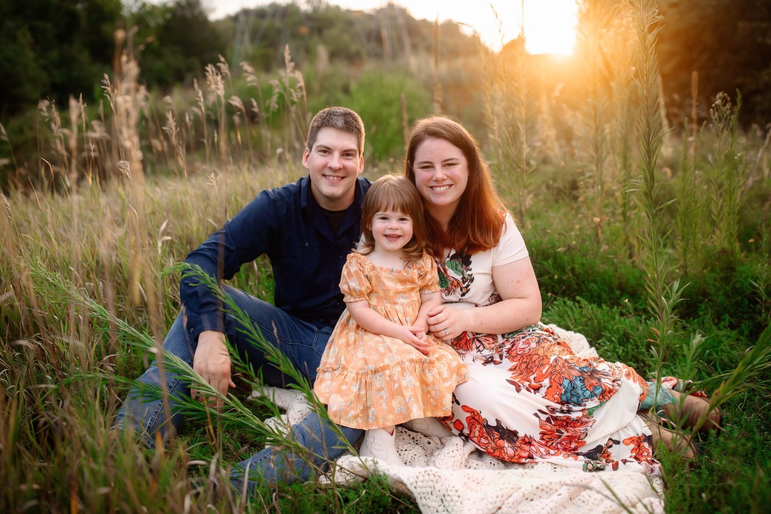 A family sitting on blanket in tall grass field during golden hour.