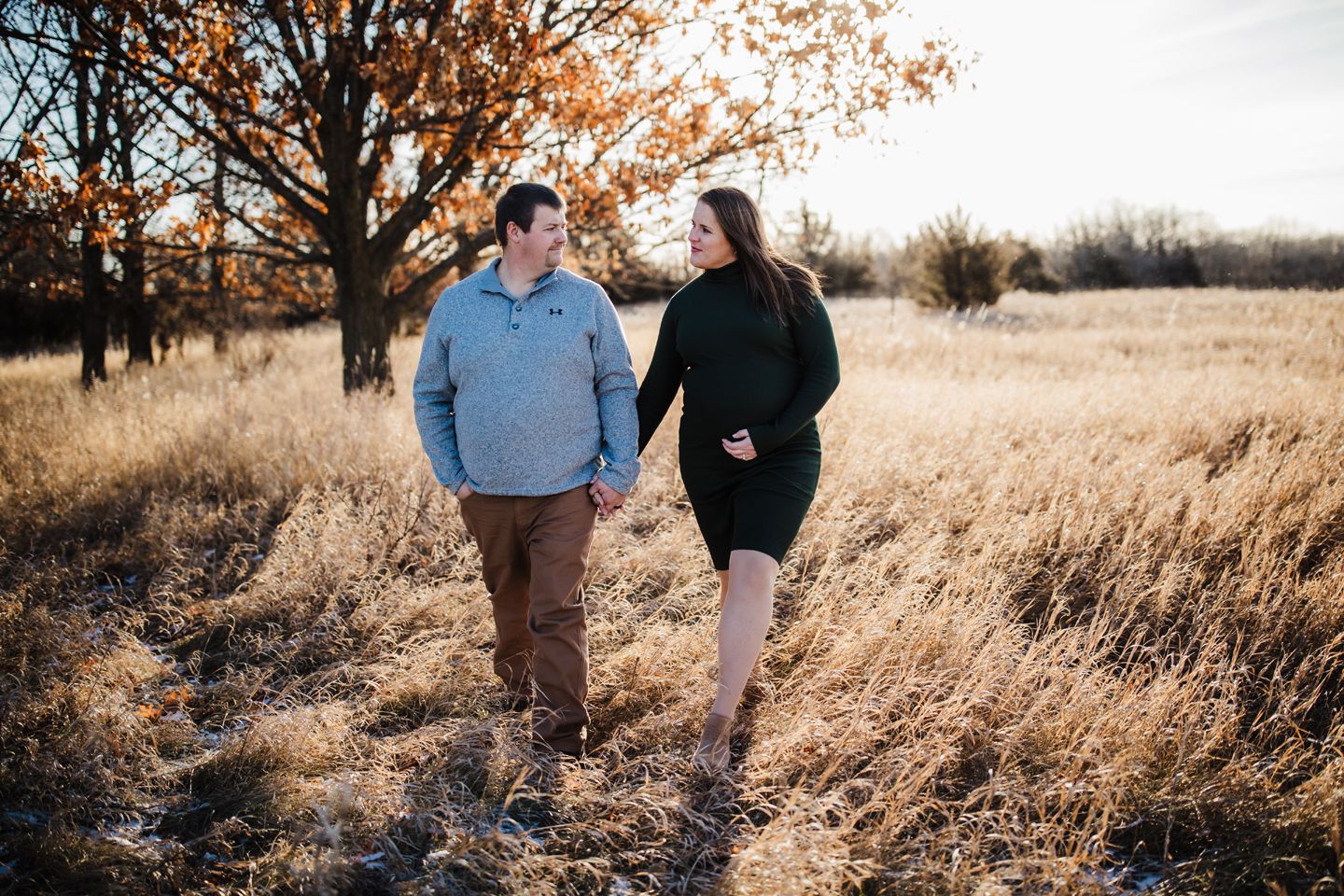 A couple walks together through golden autumn grass at sunset in a rural field.