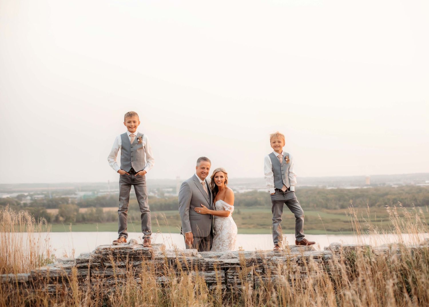 Wedding party portrait on stone wall with lake view at sunset.