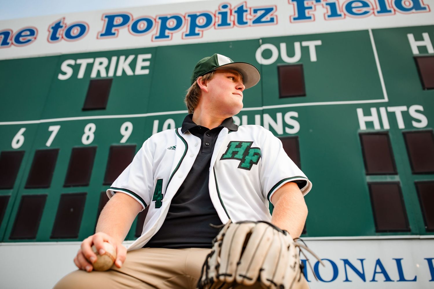 Baseball player poses beneath scoreboard at Poppitz Field.