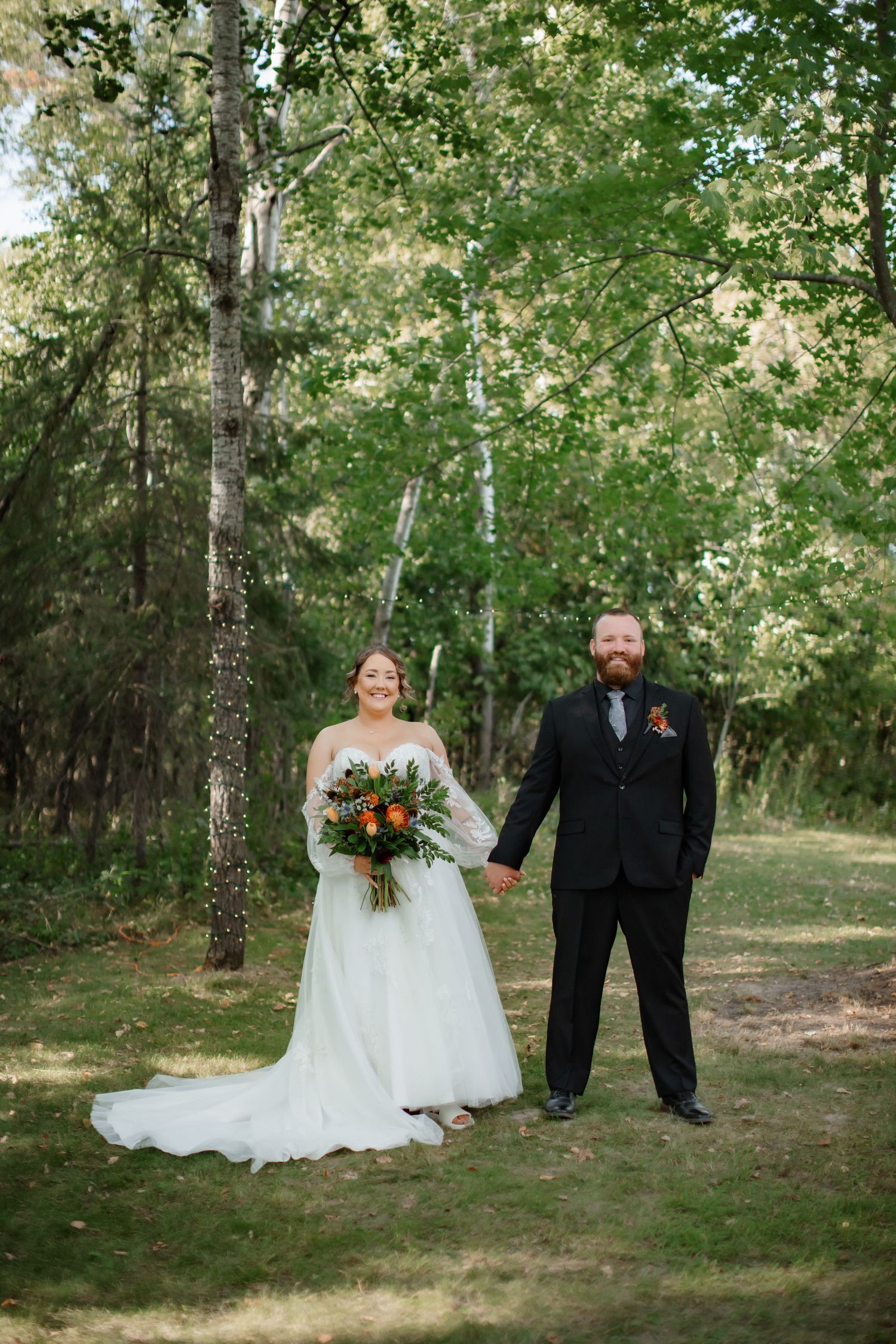 Wedding portrait in a serene forest setting with natural sunlight filtering through birch trees.