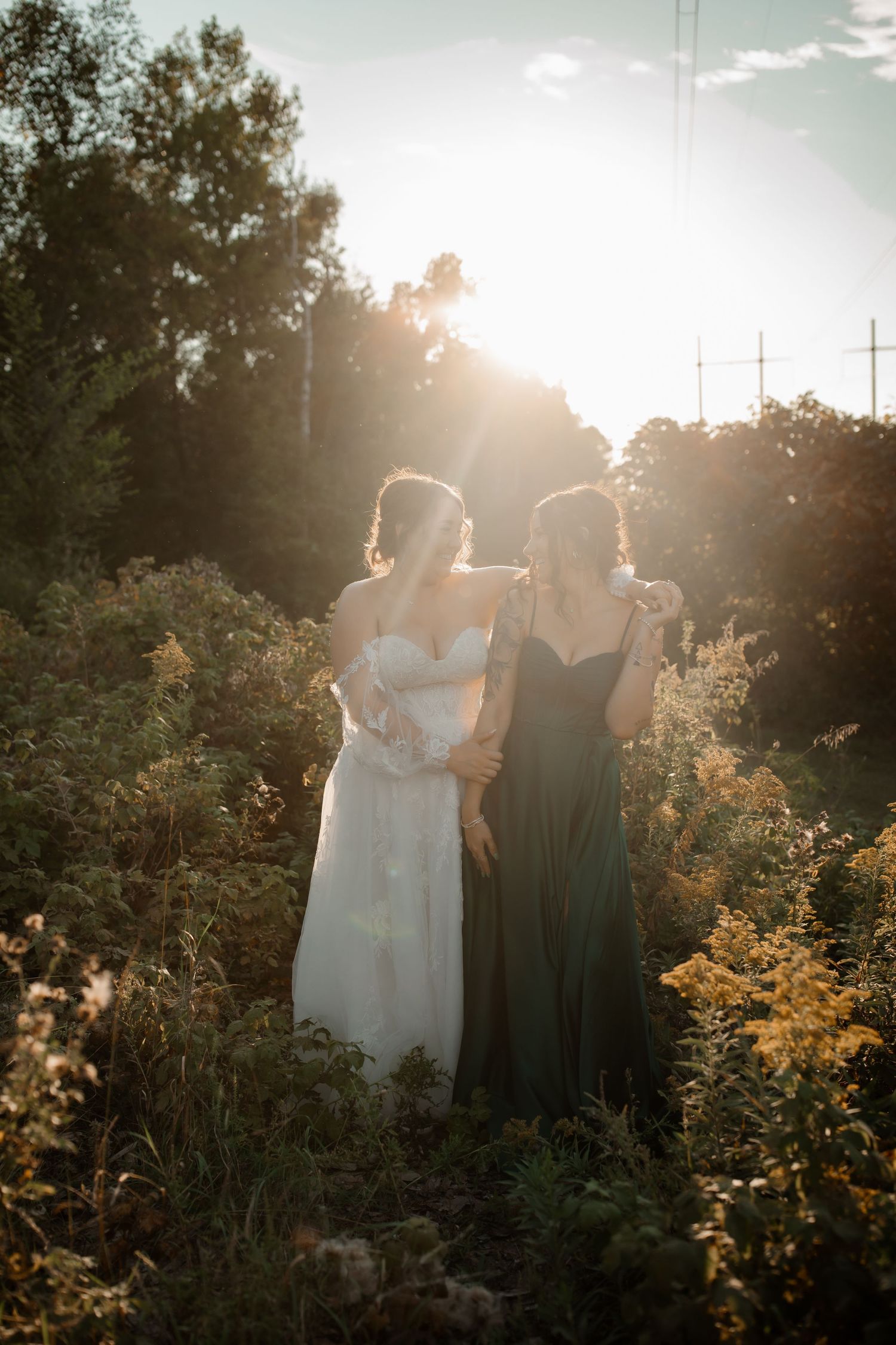 Artistic backlit sunset photo of bride and bridesmaid among golden wildflowers.