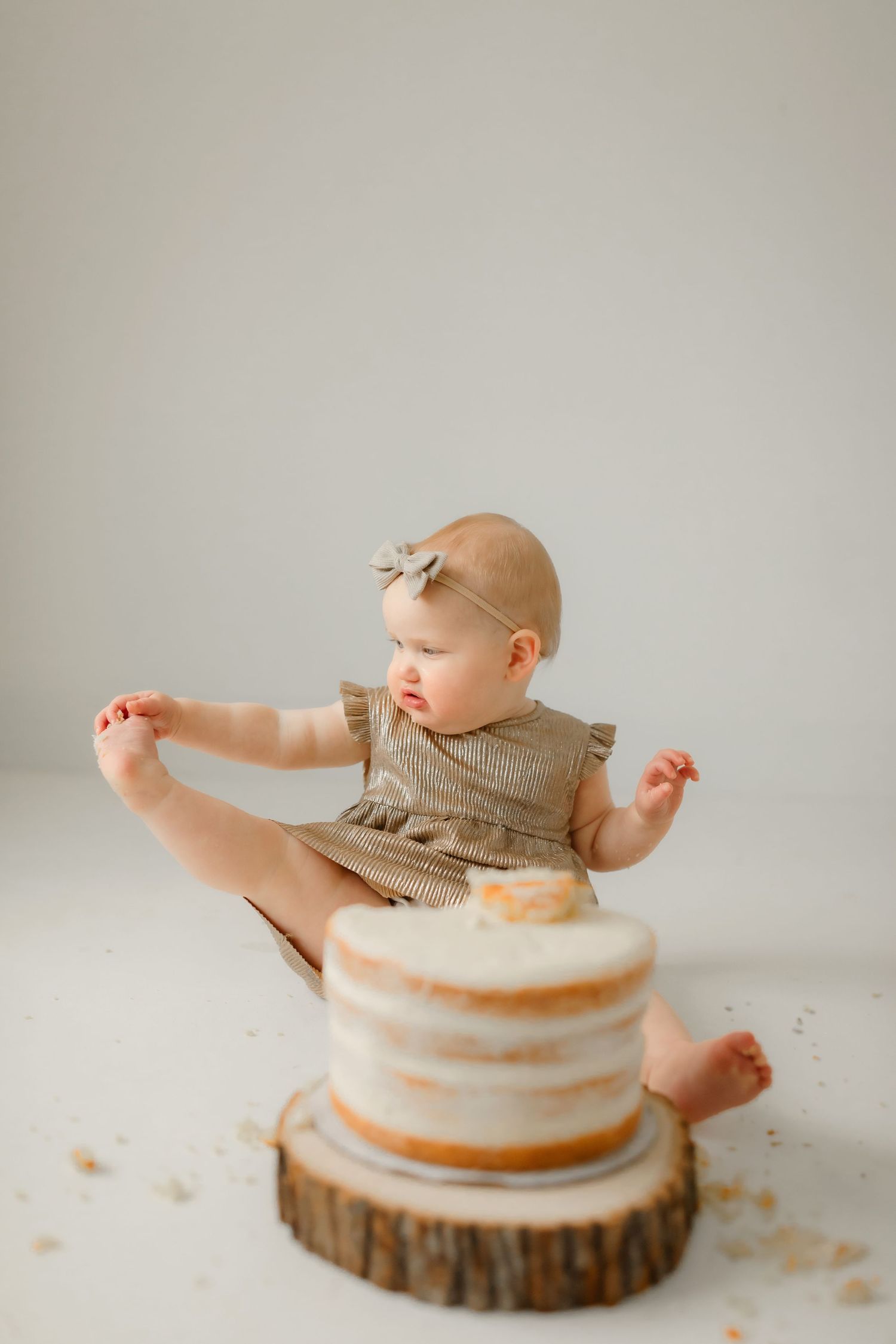 Baby having fun during cake smash session with white tiered cake on wooden stand.