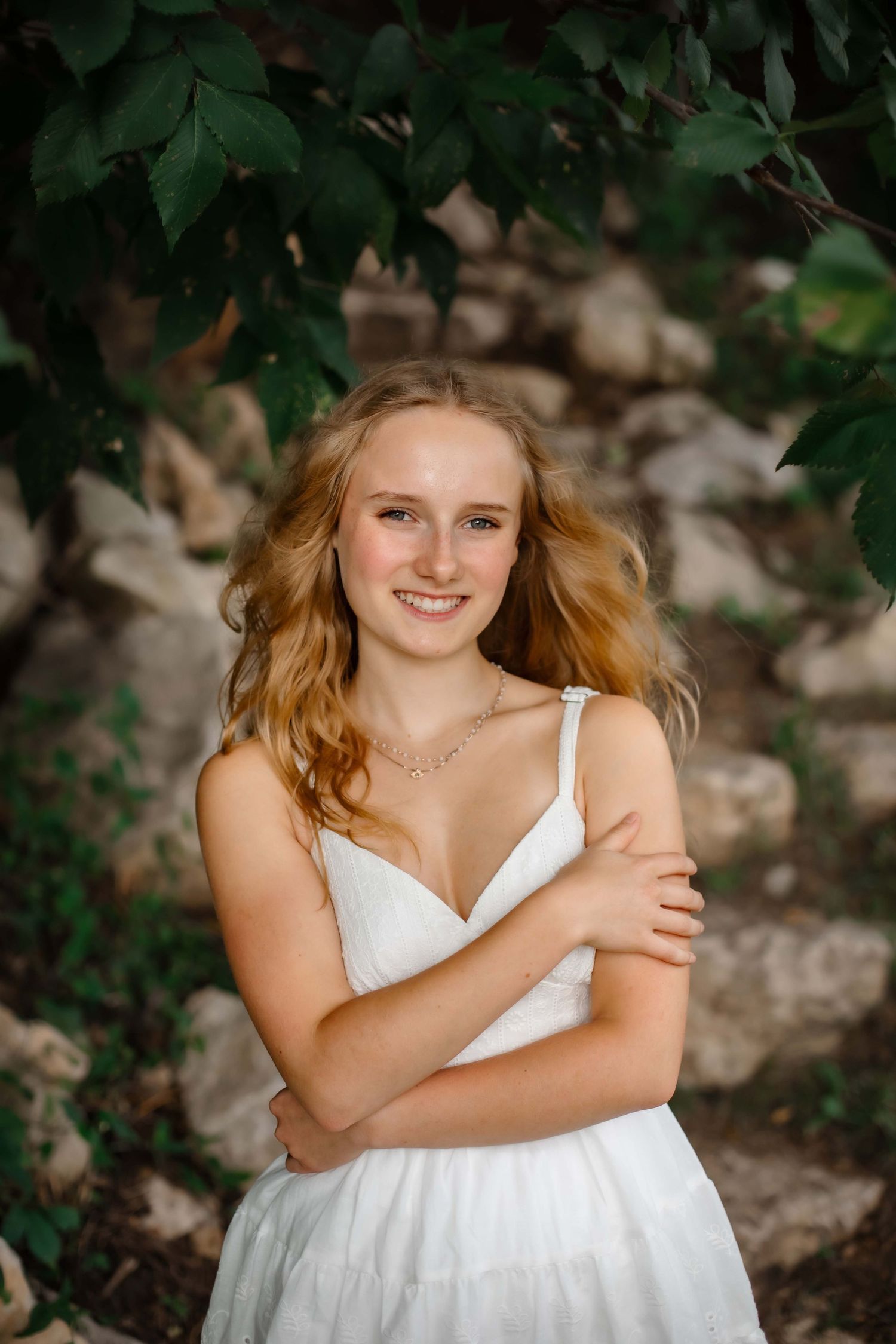 Natural portrait among green foliage wearing white summer dress.