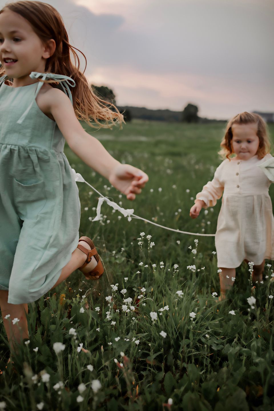 Children playing with kites in a meadow filled with white wildflowers at sunset.