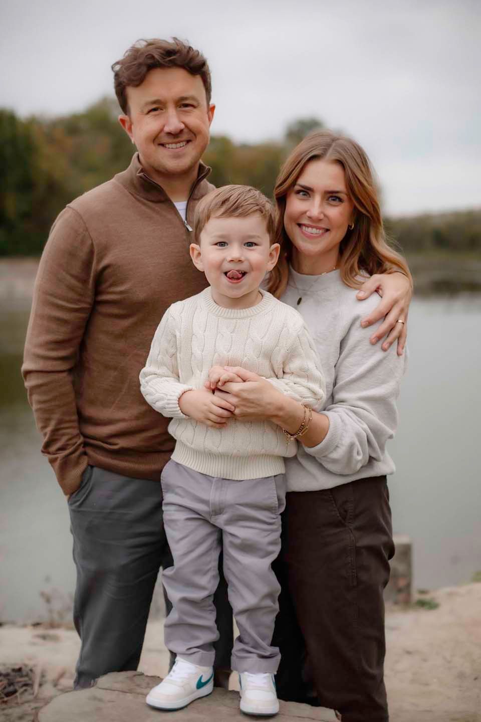 A family poses together by a lake on an overcast autumn day.