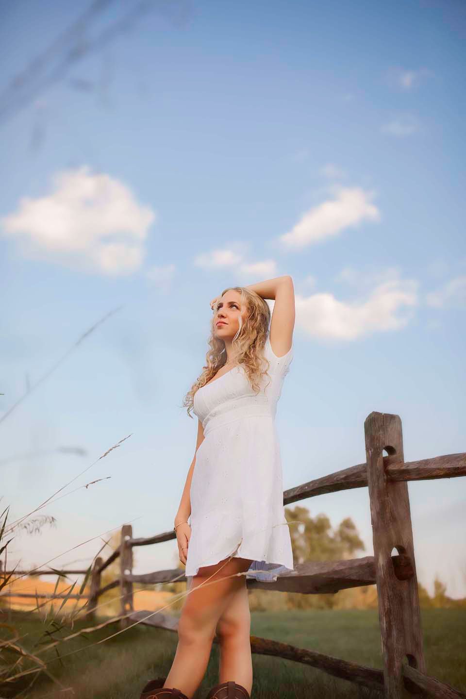 White summer dress against rustic wooden fence under blue sky with fluffy clouds.