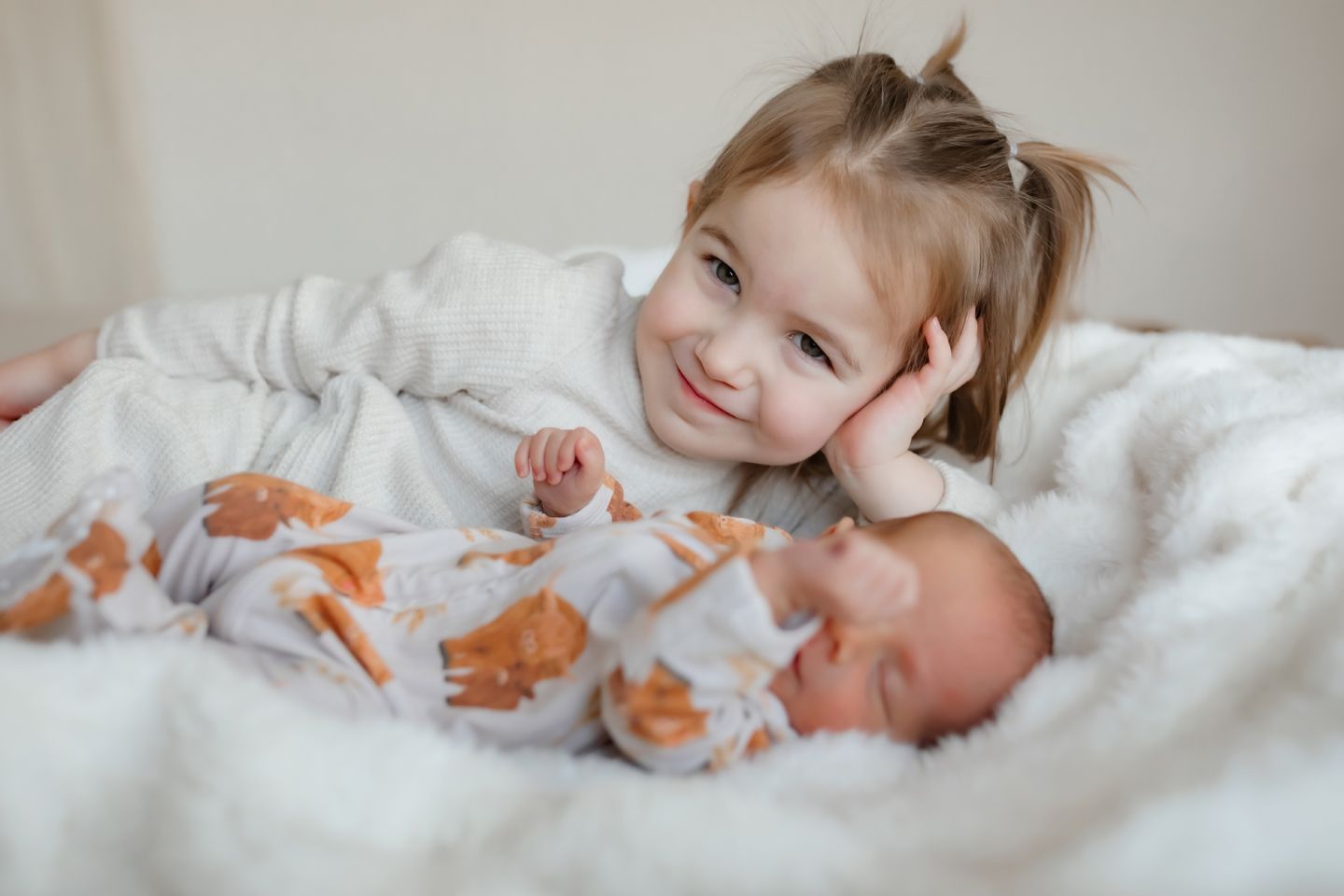 Siblings share a tender moment together on white bedding.