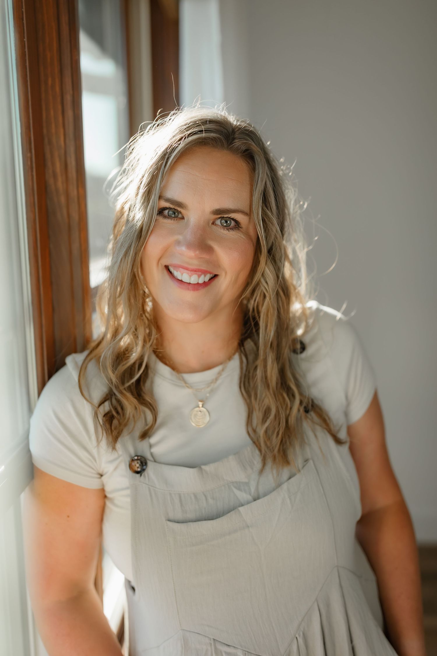 Natural lifestyle portrait in white t-shirt and gray overalls near window.
