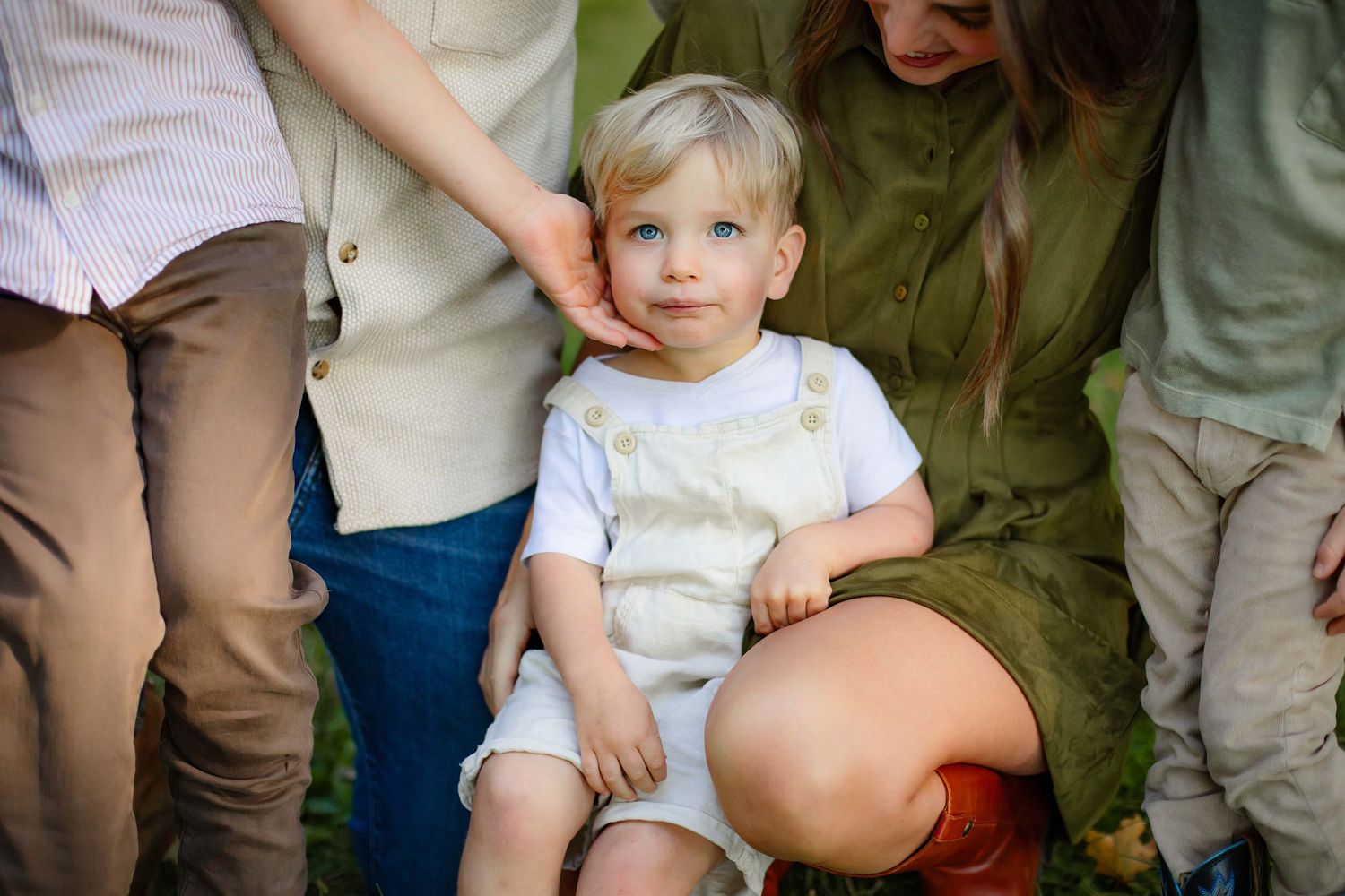 A young child sits between adults wearing casual clothing during an outdoor family photo session.