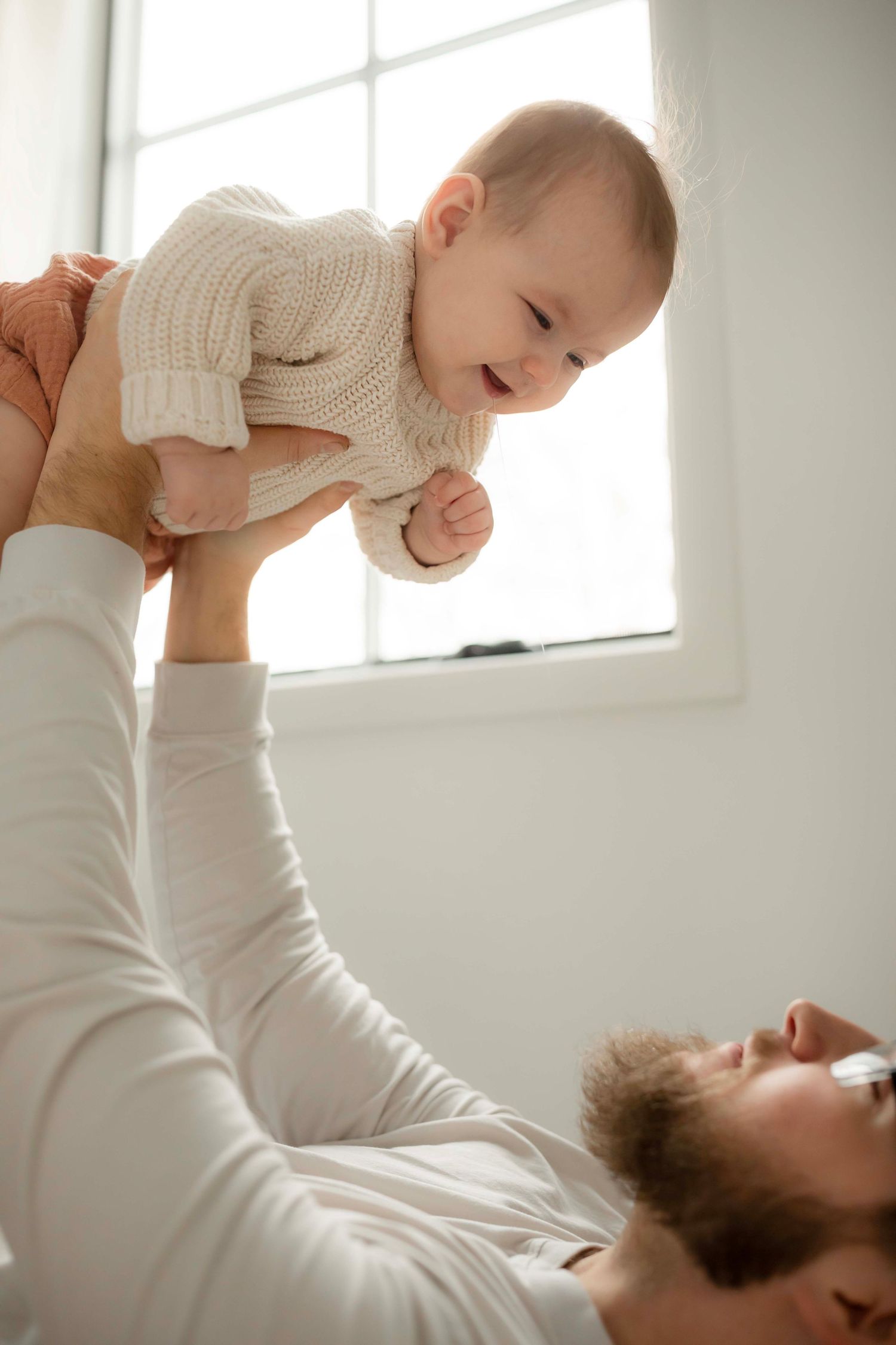 Parent and baby share a joyful moment playing together in a bright white room.