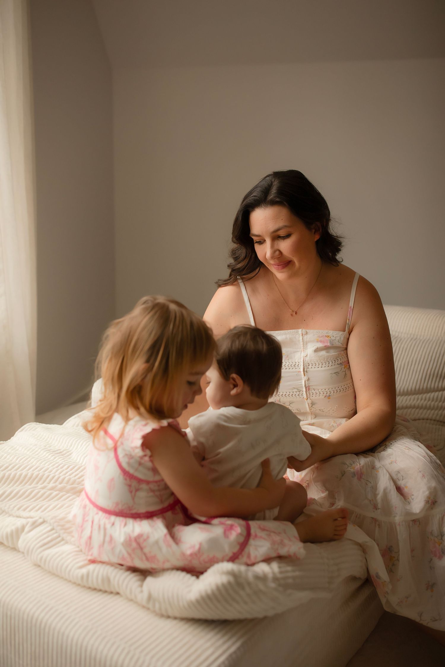 A series of tender moments captured between a mother and children sitting together on a white couch in soft lighting.