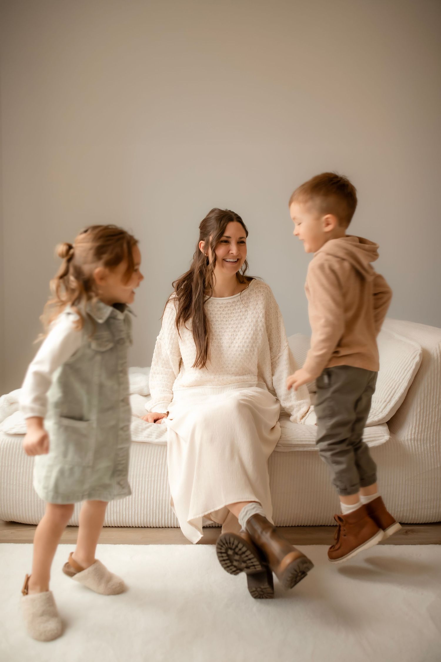 A sequence of four photos showing children playing and jumping on a white couch in neutral-toned clothing.