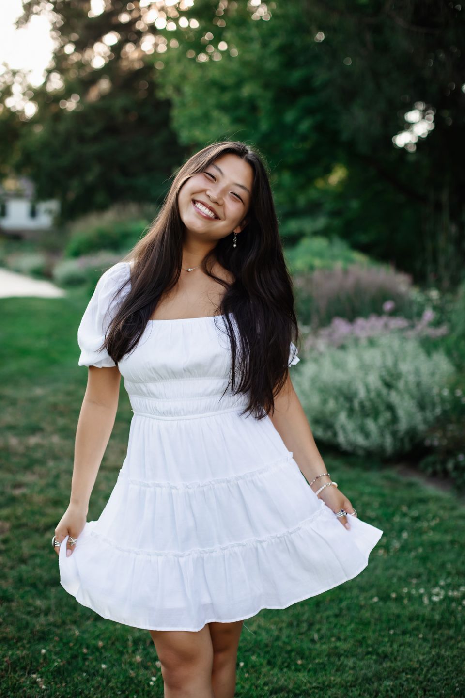 A person wearing a white summer dress twirls with joy in a garden setting at sunset.