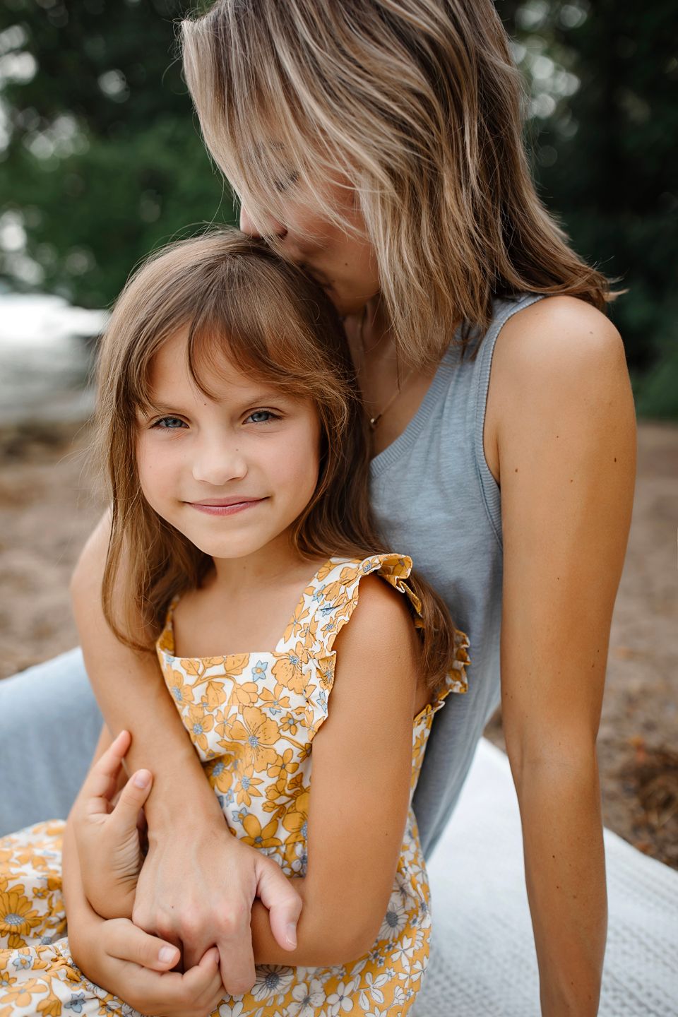 A caring embrace between two people outdoors, with one wearing a yellow floral dress and the other in gray.