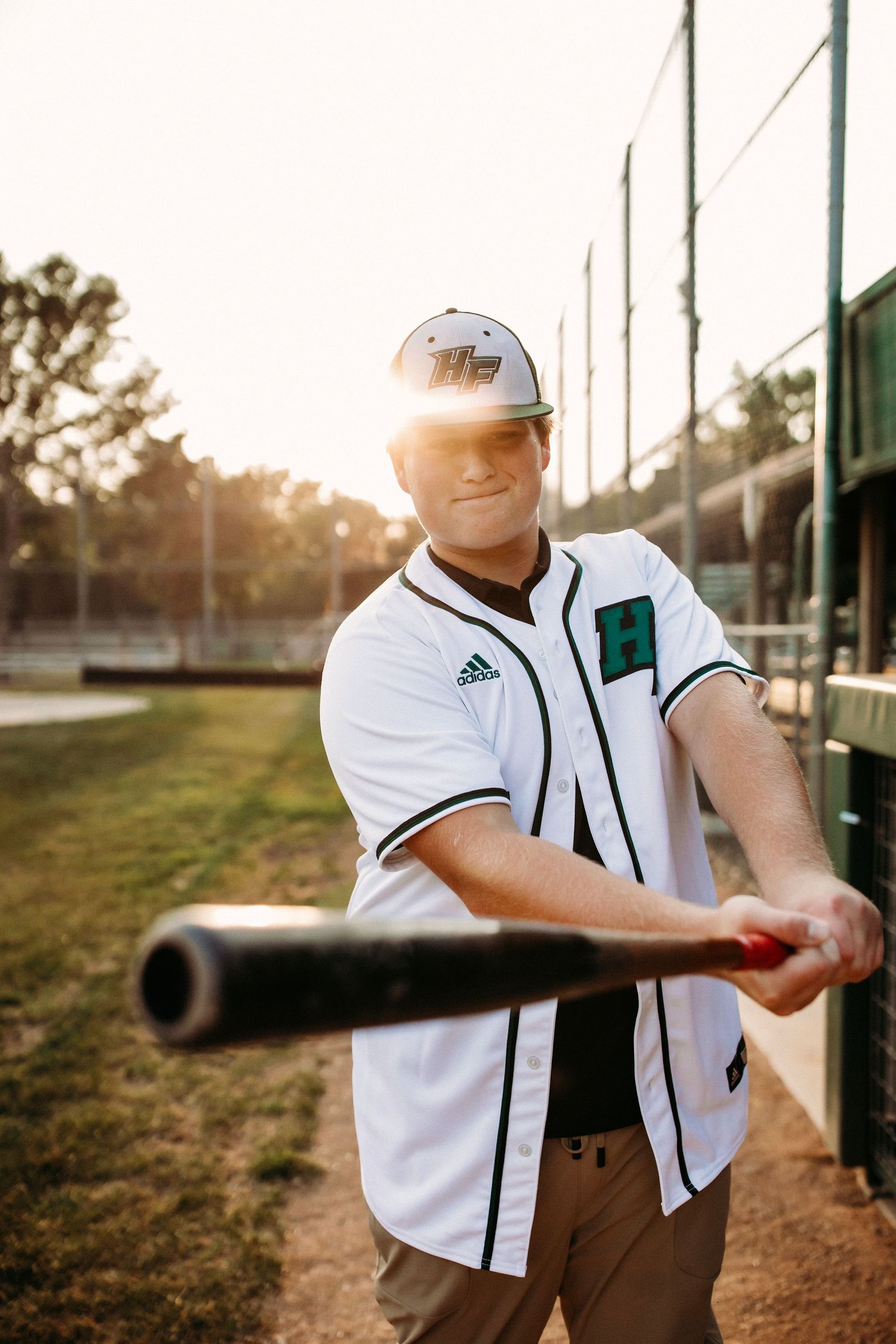 Baseball player practicing swing with bat during sunset on field.