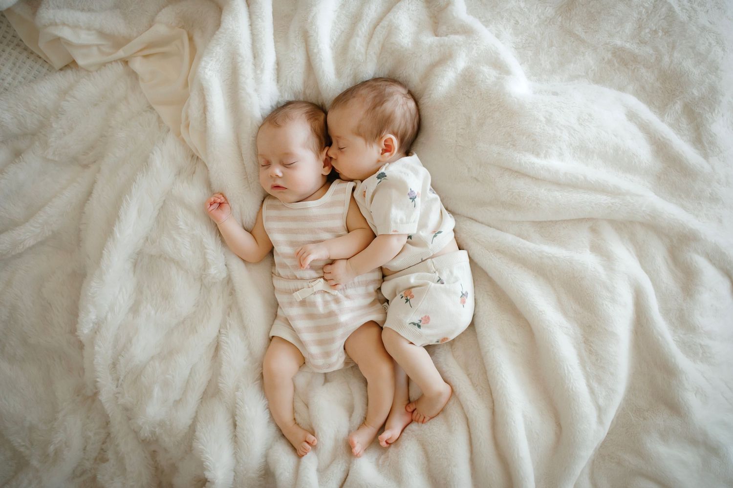 Two sleeping infants lying side by side on white bedding.