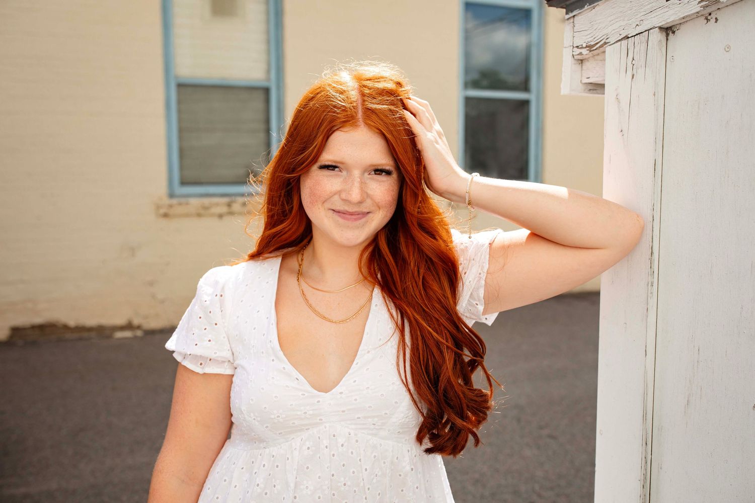 Beautiful long red hair flowing in natural light against a neutral building exterior.